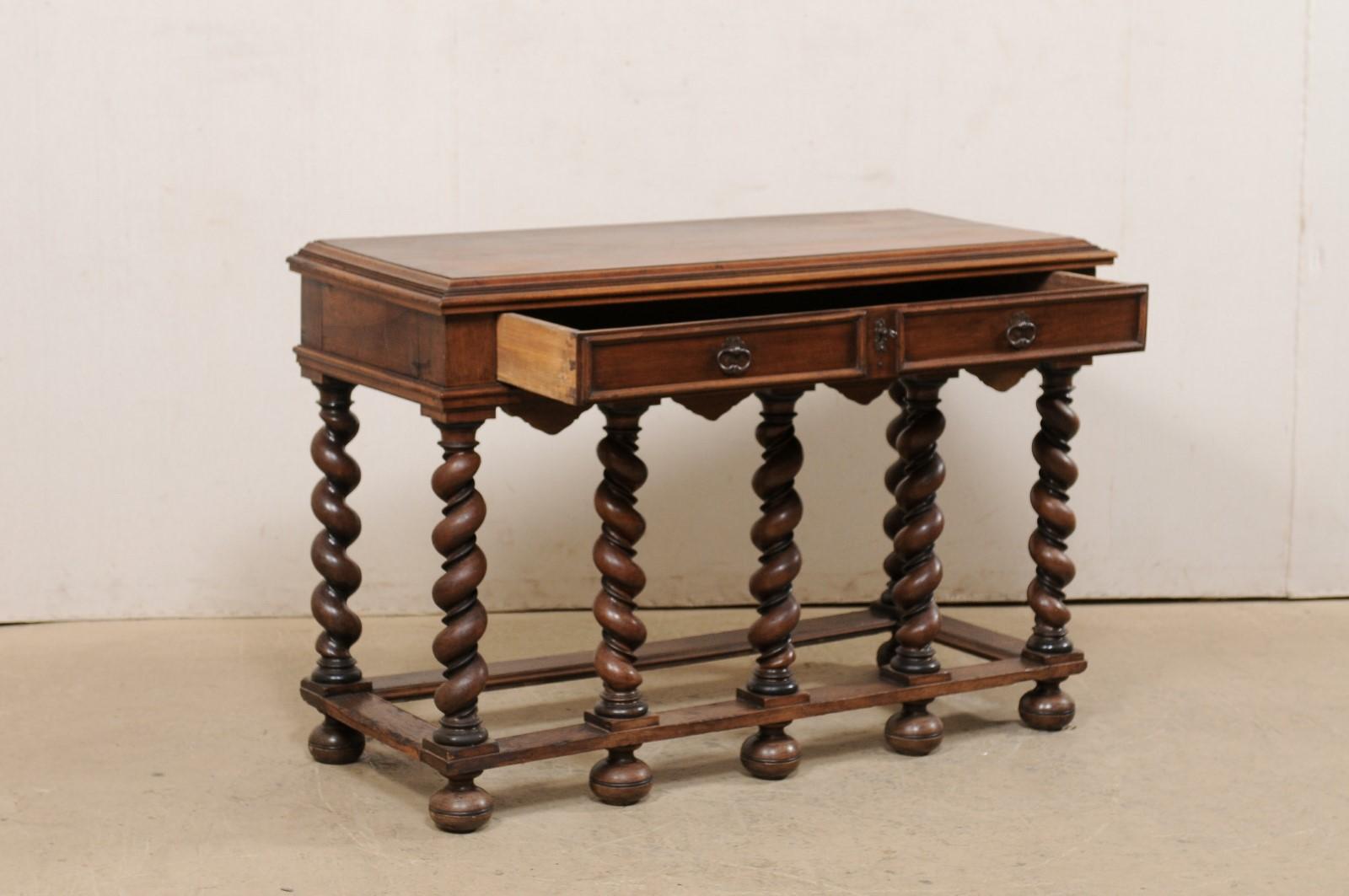 An English wood table with barley twist legs from the early 20th century. This antique table from England features an elongated rectangular top, which rests atop an apron that houses a pair of panel-front drawers at one side, and is beautifully