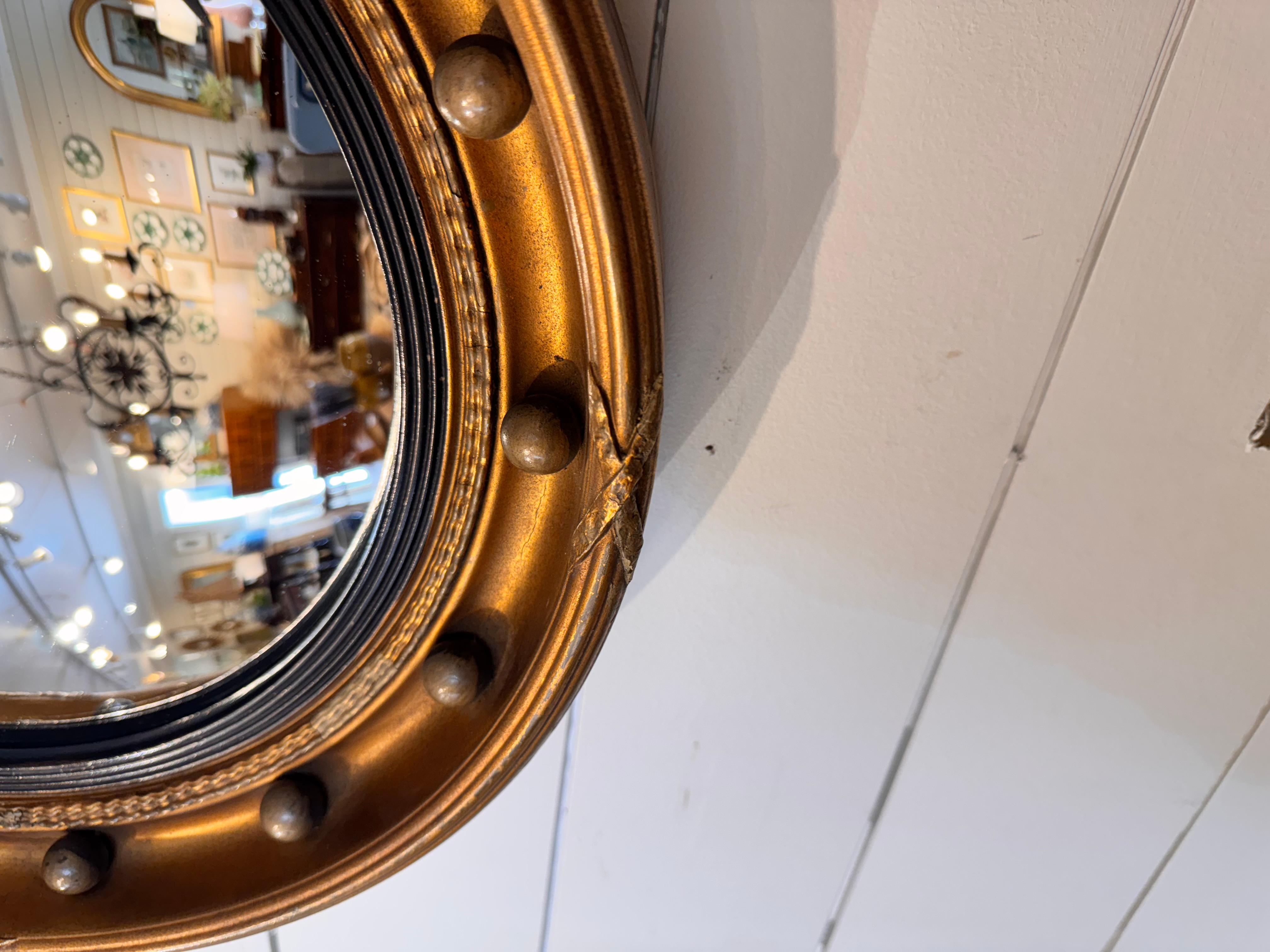This antique English Federal convex wall mirror would be a lovely statement piece for any space in your home. It is finished with gilt-wood gold finish, rivets and lovely eagle topper. It's a late 19th century piece in excellent condition with only