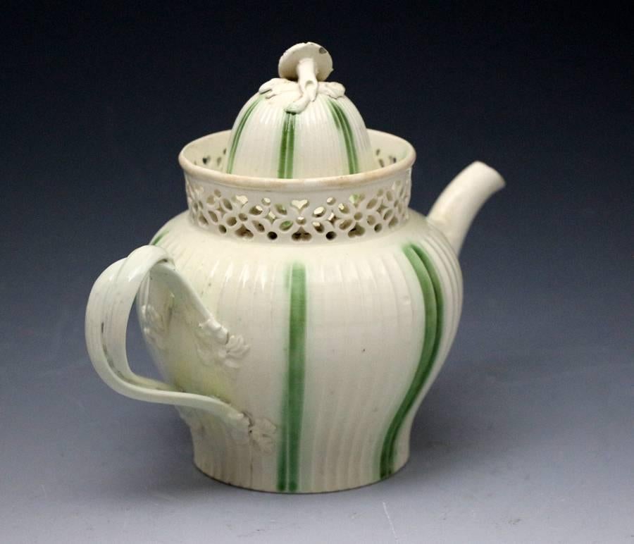 Late 18th century English creamware pottery teapot decorated with underglaze green stripes with a reticulated rim, the dome shaped cover has a flower head and leaf finial and the handle is a classic double strap form.
