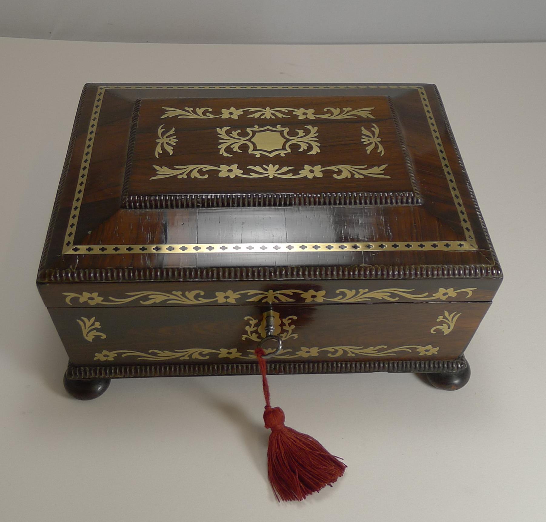 A truly elegant table / desk box, English in origin and from the Regency period dating to circa 1820.

Standing on four original bun feet, the box is veneered in exotic rosewood and the top and front is beautifully inlaid with cut brass