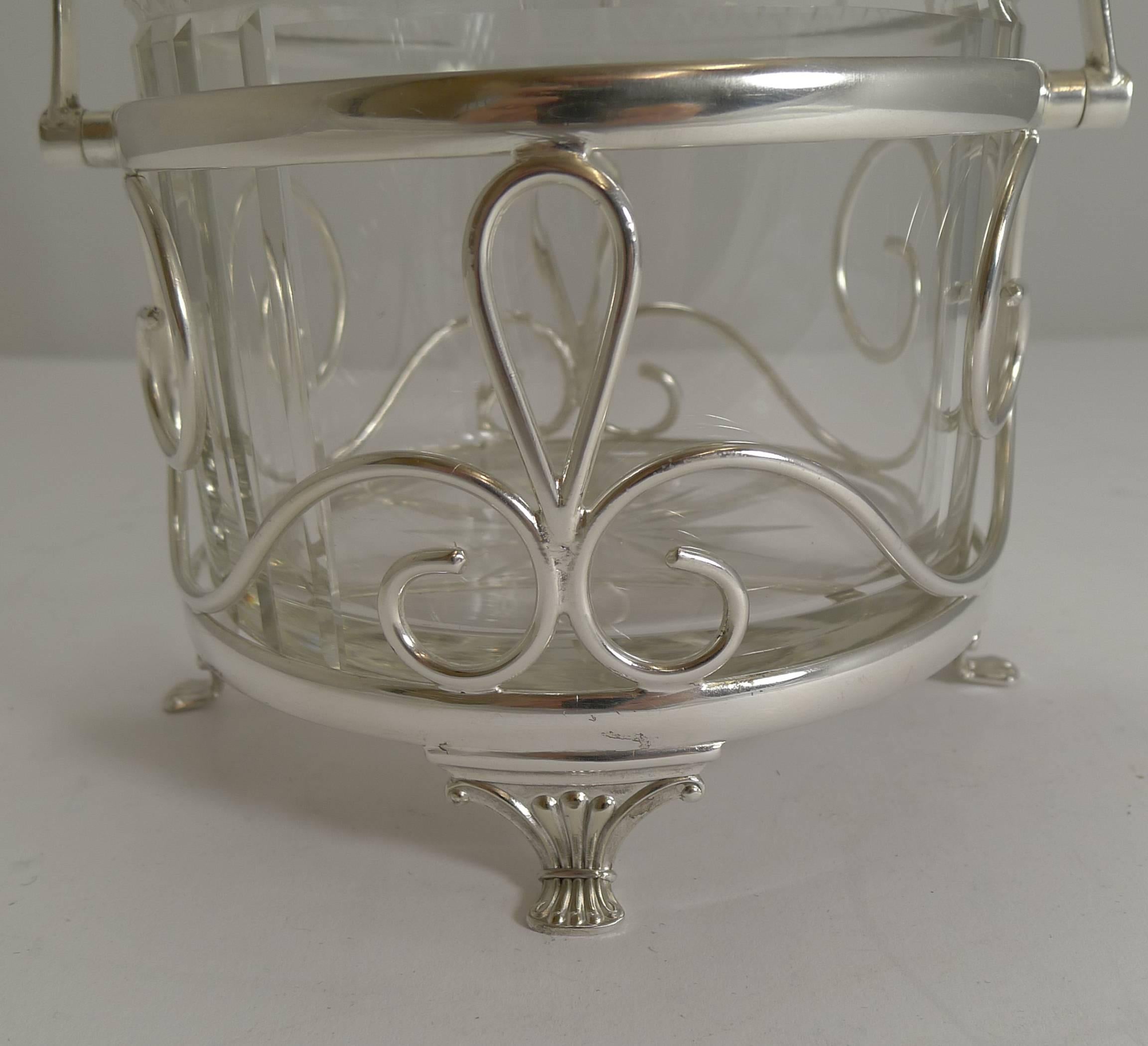A wonderfully decorative biscuit box, the frame made from EPNS (Electro-plated nickel silver) and fully marked by the Birmingham silversmith, Arnold E Williams, it stands on four pretty feet.

The box itself is made from a hefty piece of English
