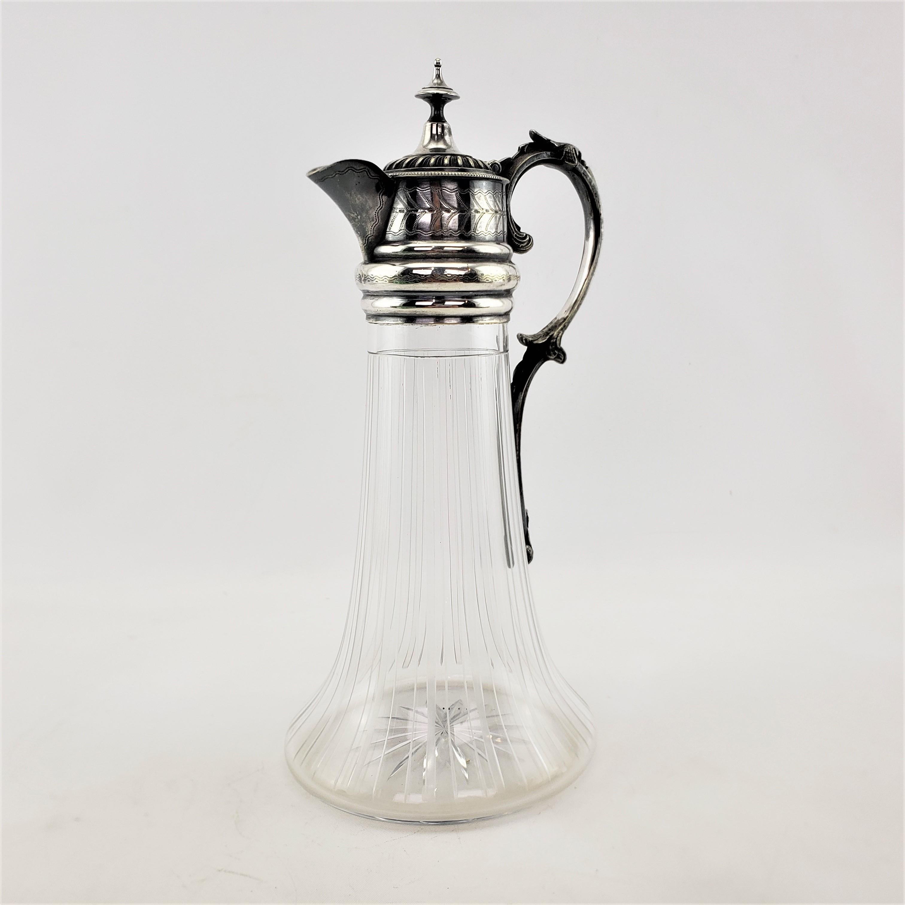 This antique cut crystal and silver plate mounted claret jug is unsigned, but presumed to have originated from England and dates to approximately 1920 and done in the late Victorian style. The claret jug is done with a tapered crystal base with cut