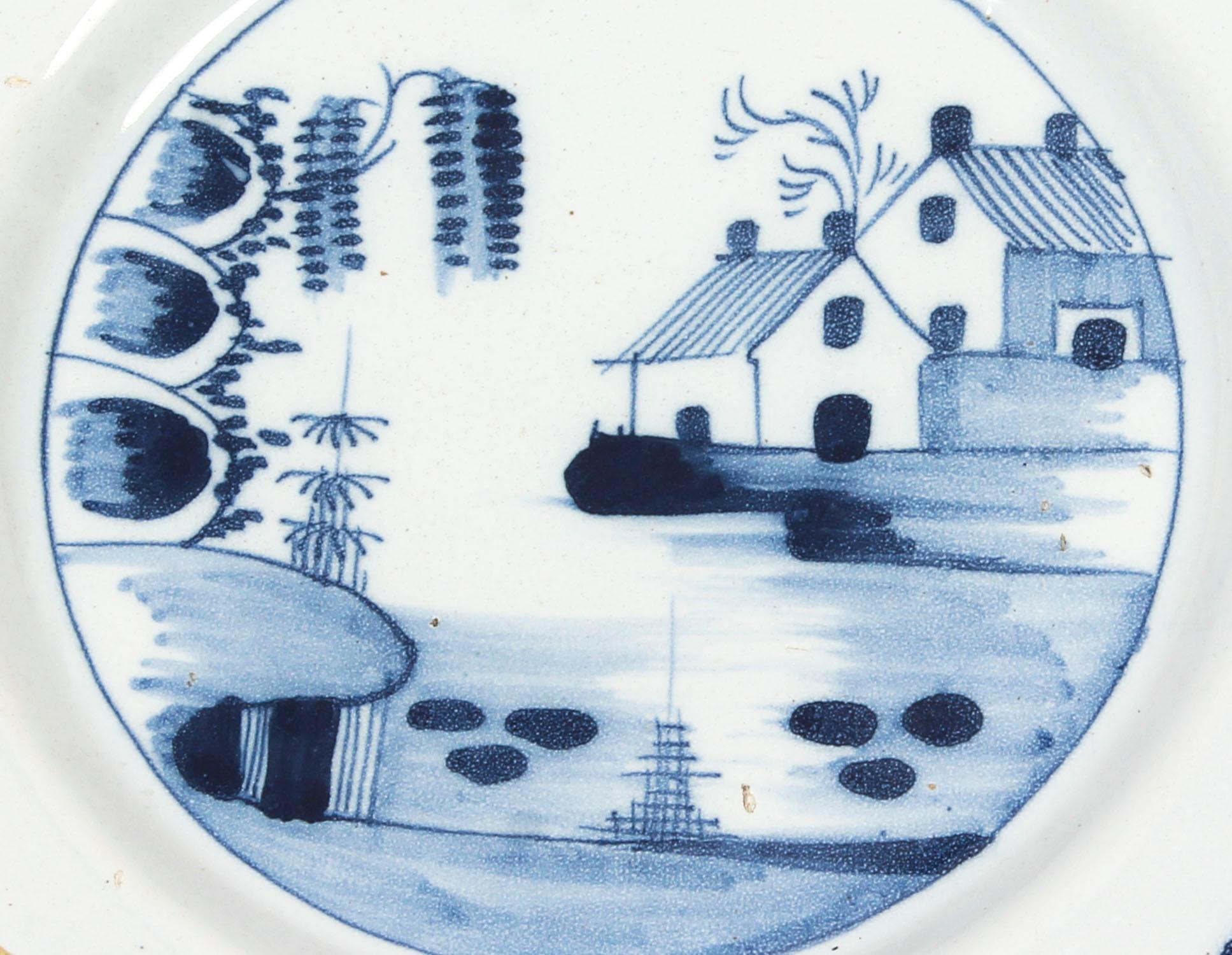 This is a beautiful antique English Delft blue and white decorated plate cabinet plate, circa 1780 in date.

English delft blue and white dish, decorated with houses on a bank of a river with a mimosa tree hanging over the side, inspired by the