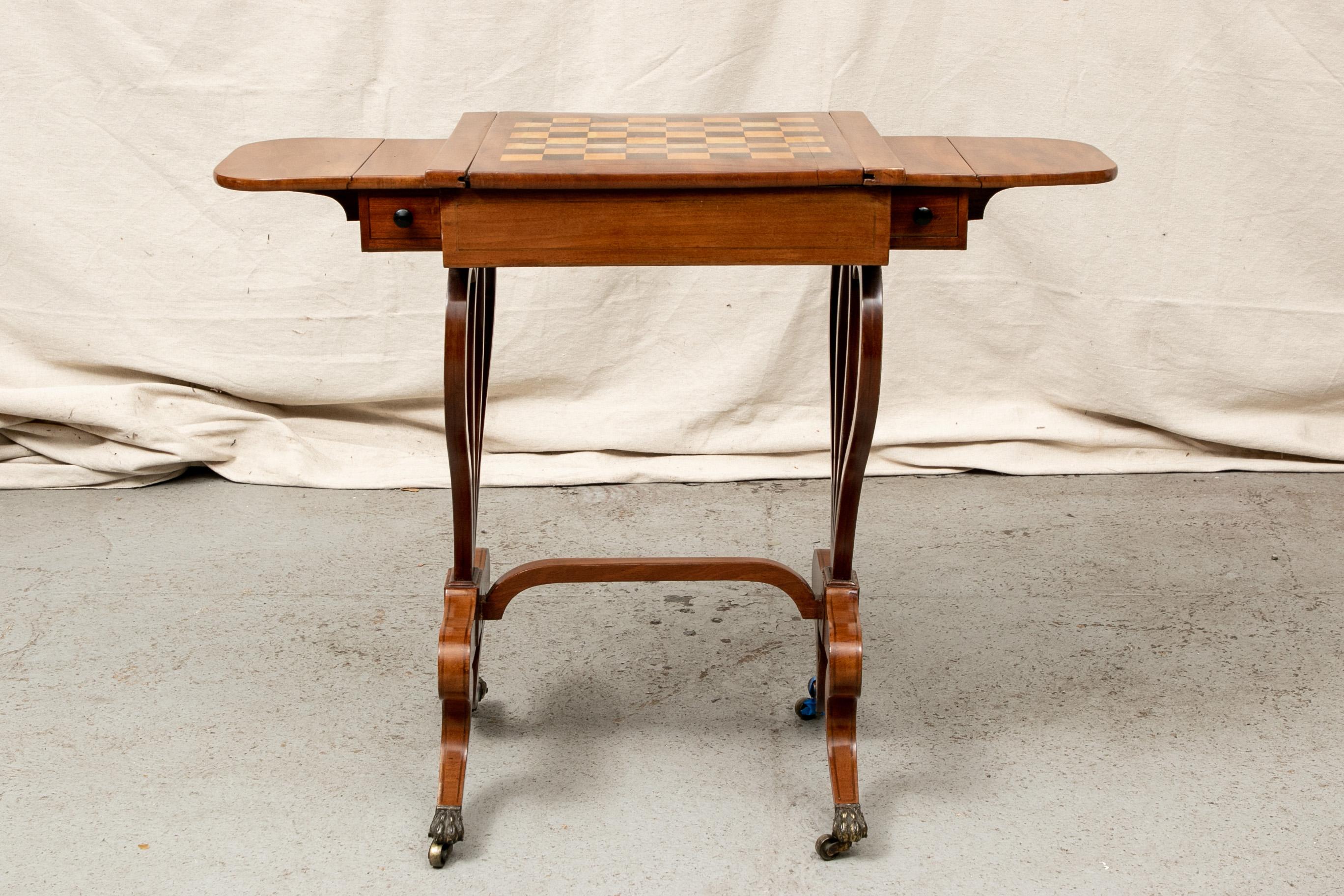 Antique English diminutive drop leaf games table, Mahogany with a square dark green leather top reversing to a mixed wood game board. Inside is a colorful leather backgammon board. The side drawers with drop leaves, the whole raised on curved lyre