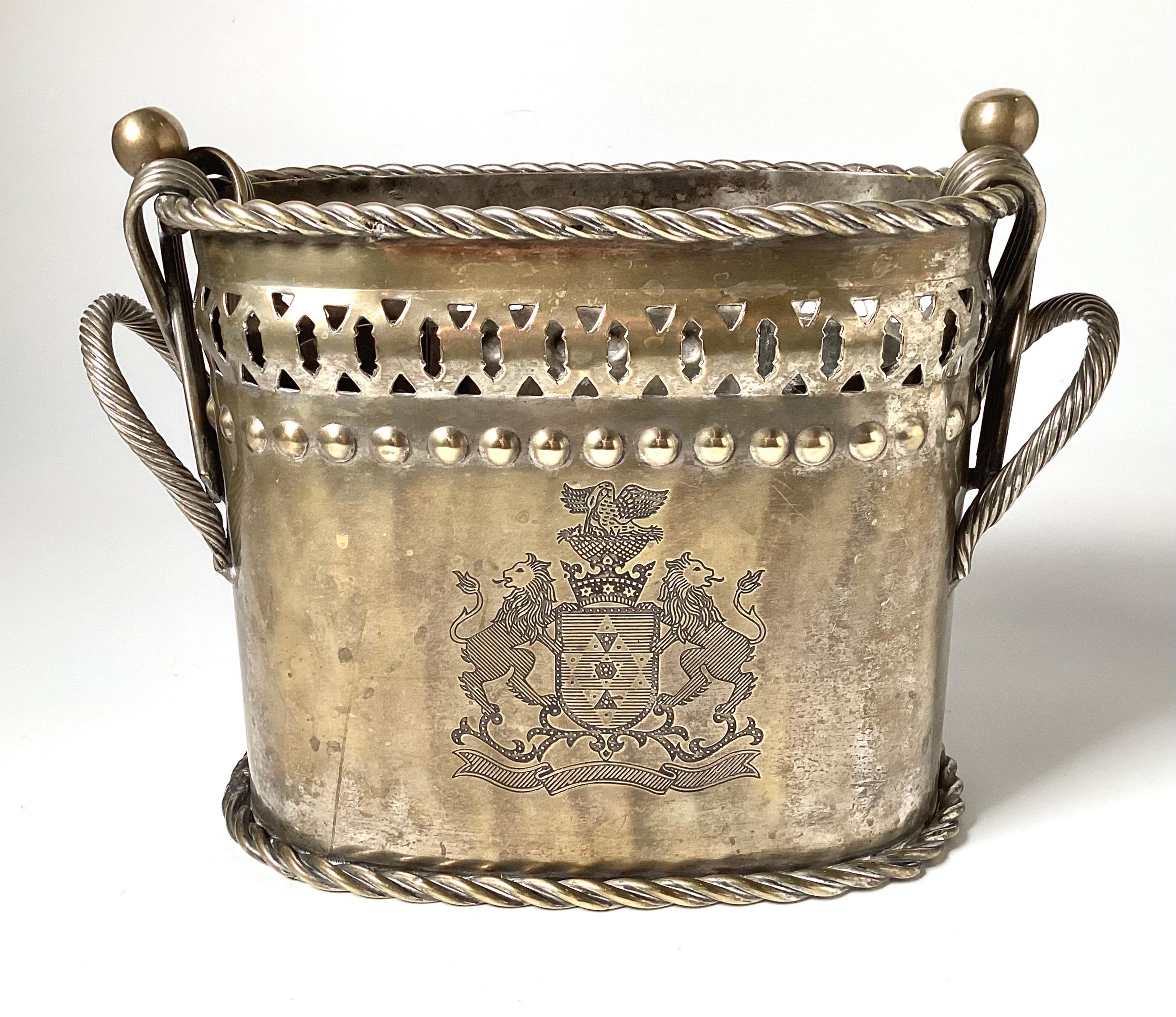 An Antique English wine holder in a worn silvered brass. The The front with an Armorial engraved crest. The brass base with some silvering on the surface.