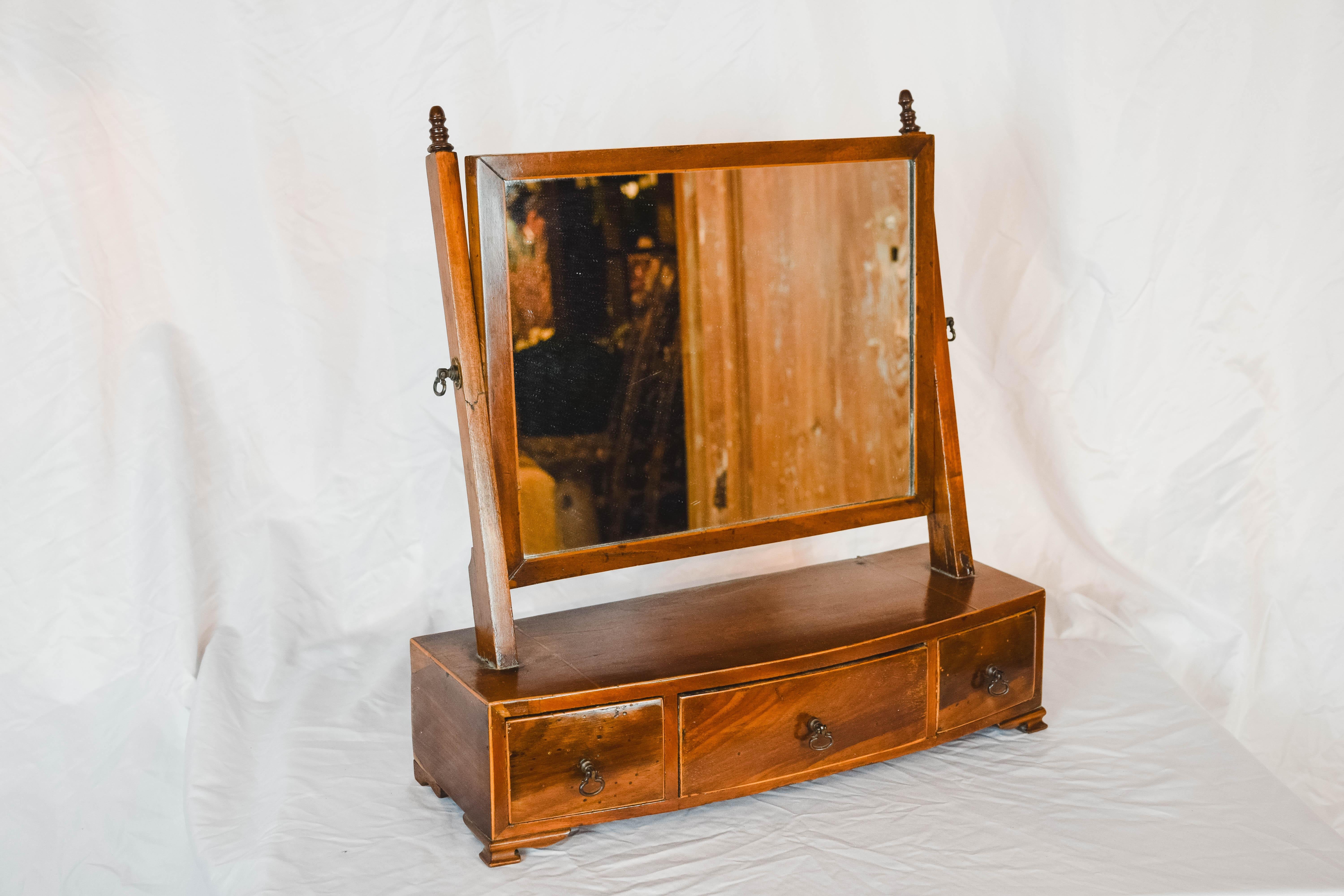 This antique English dressing table mirror is in good condition. Displaying good color throughout. The wood is believed to be Mahogany. The mirror is original and adjustable. The base is on bracket feet. A suite of three, oak lined, shaped drawers