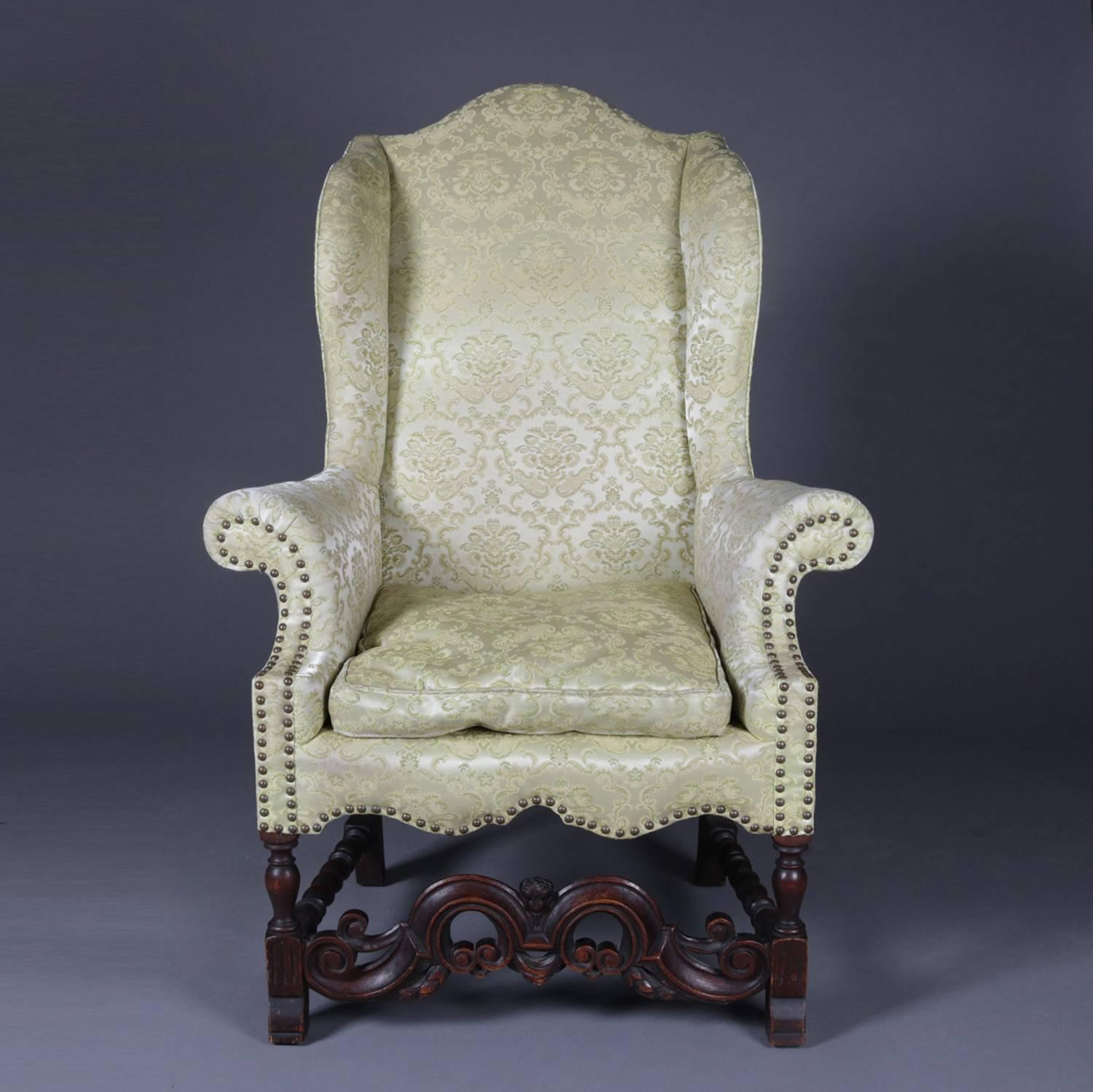 Antique English Edwardian upholstered wingback armchair features scalloped skirt and scrolled arms, carved mahogany frame with pierced foliate and scroll form front stretcher with barley twist side stretchers, circa 1910

Measures: 51