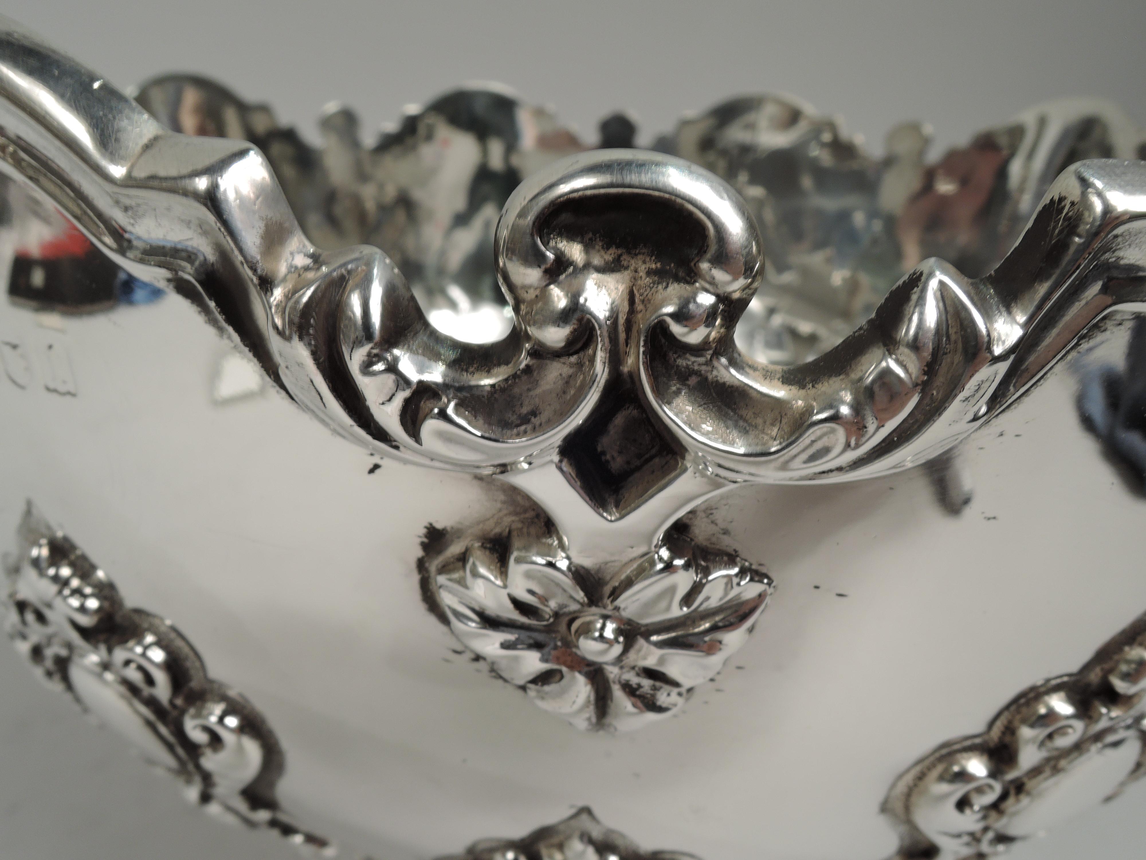Edwardian Georgian sterling silver monteith bowl. Made by William Hutton & Sons, Ltd in London in 1906. Round and curved on raised and stepped foot. Molded curvilinear rim with interspersed with leaves and applied pendant flowers. Vertical strapwork