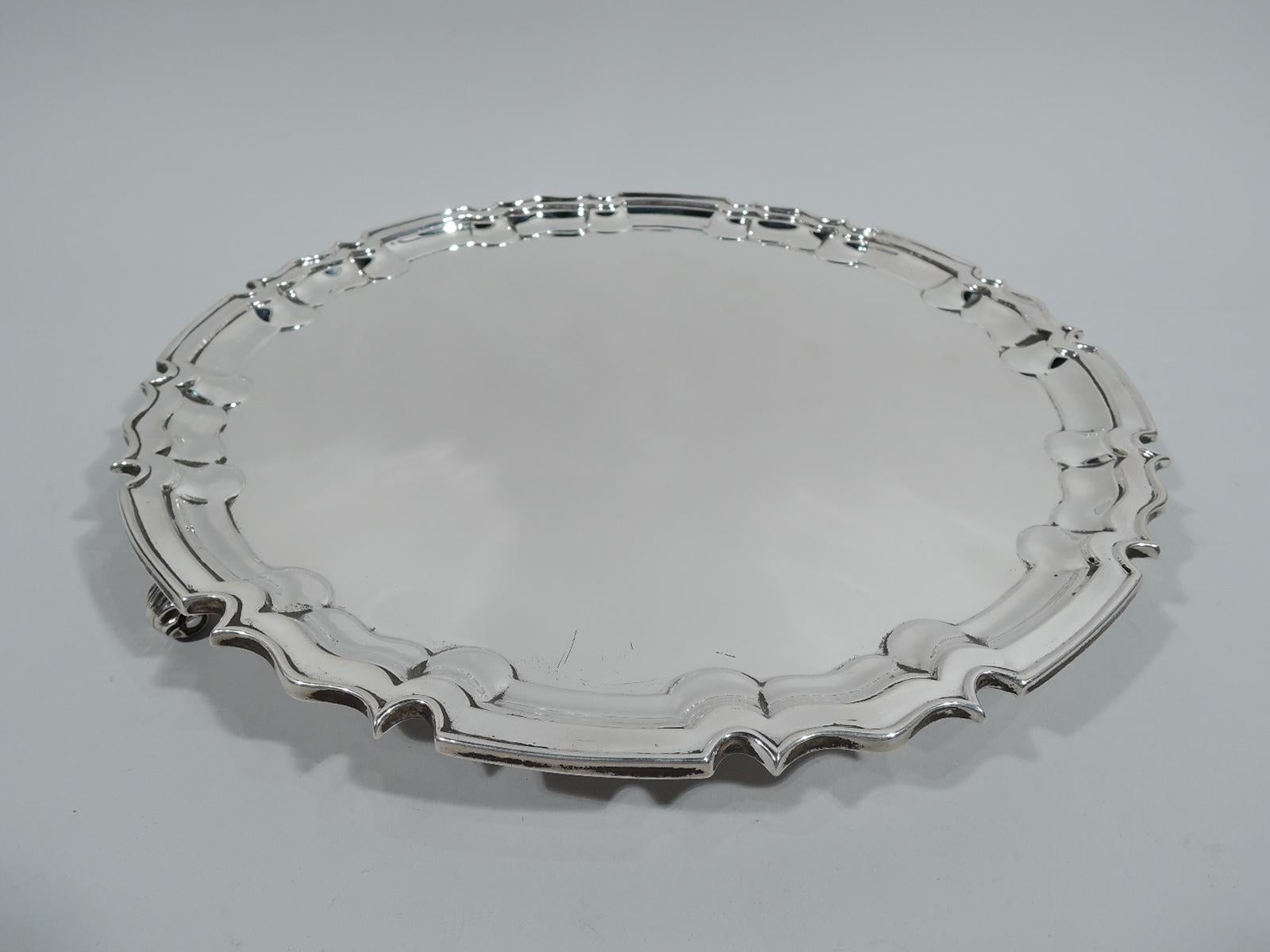 Edwardian Georgian sterling silver salver. Made by William Hutton & Sons, Ltd in London in 1905. Round with crisp and molded curvilinear piecrust rim. Three leaf-capped volute-scroll supports. Fully marked. Heavy weight: 33.5 troy ounces.