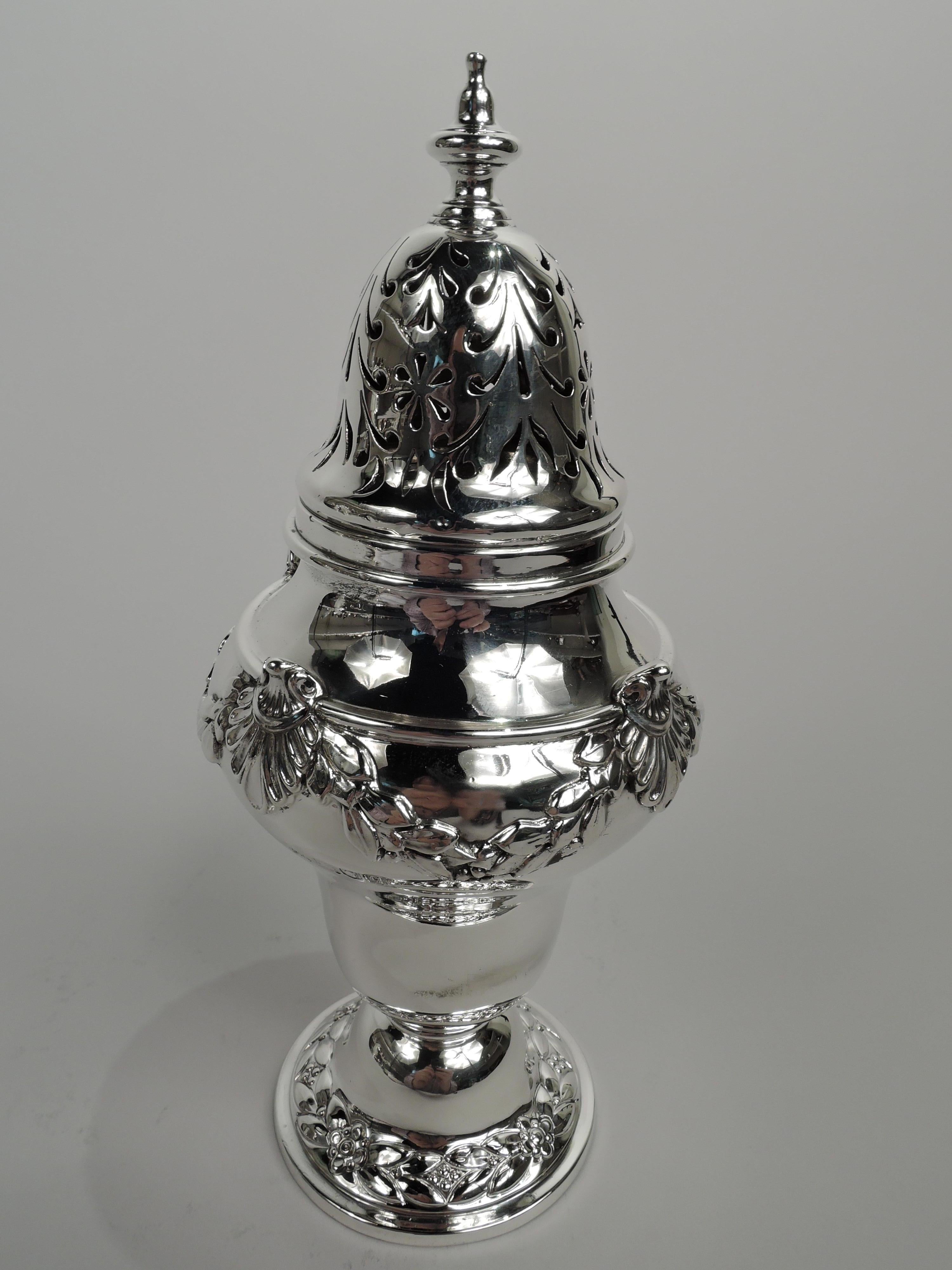 George V sterling silver sugar caster. Made by Harrison Bros & Howson in London in 1911. Baluster with applied shell-mounted garland on domed foot with chased imbricated leaf-and-flower border. Cover threaded and domed with vasiform finial and