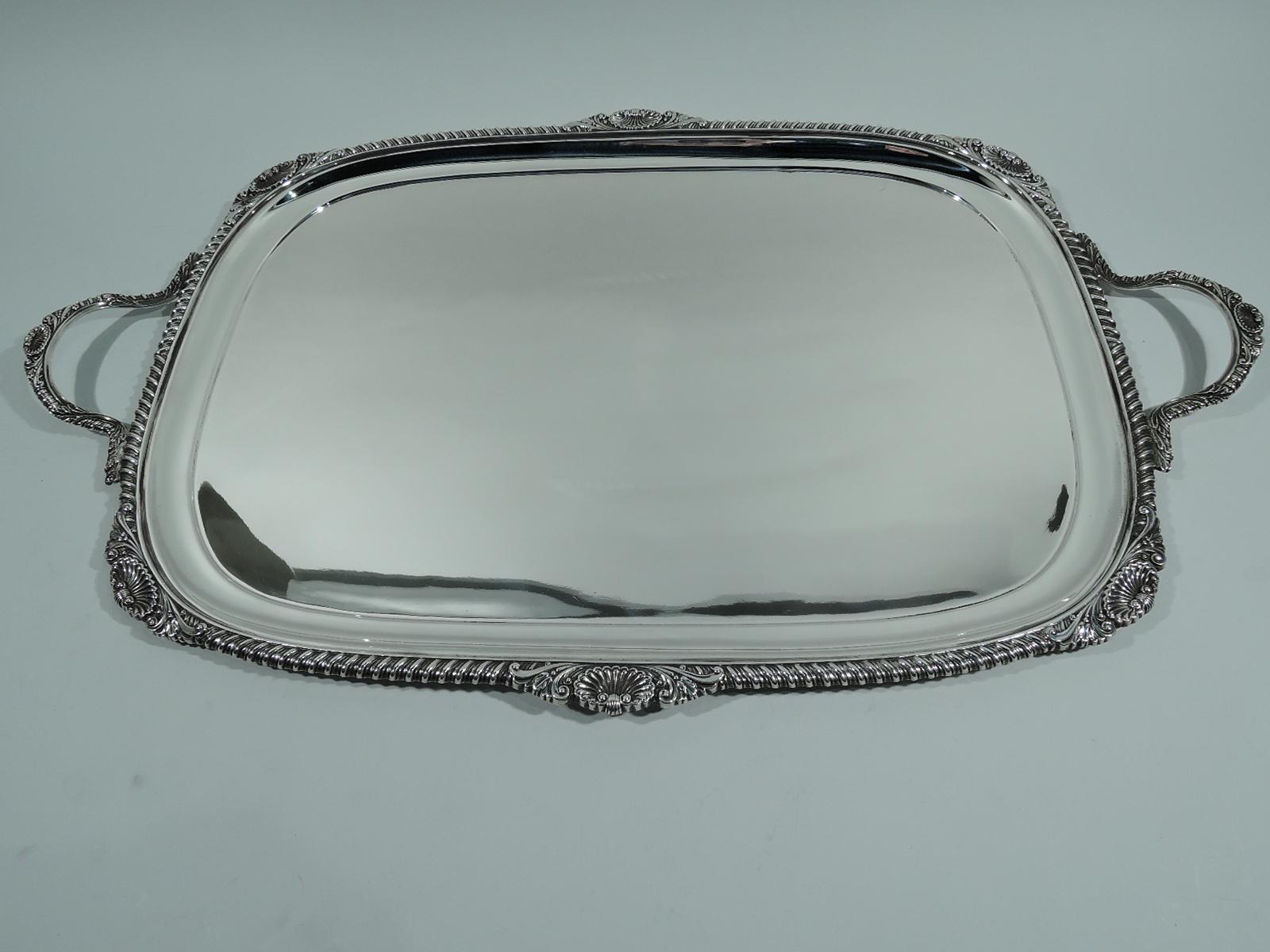 George V sterling silver tea tray. Made by William Hutton & Sons, Ltd in Sheffield in 1912. Plain and rectangular well with curved shoulder. Gadrooned rim interspersed with shells and leaves. C-scroll end handles same. Traditional and capacious with