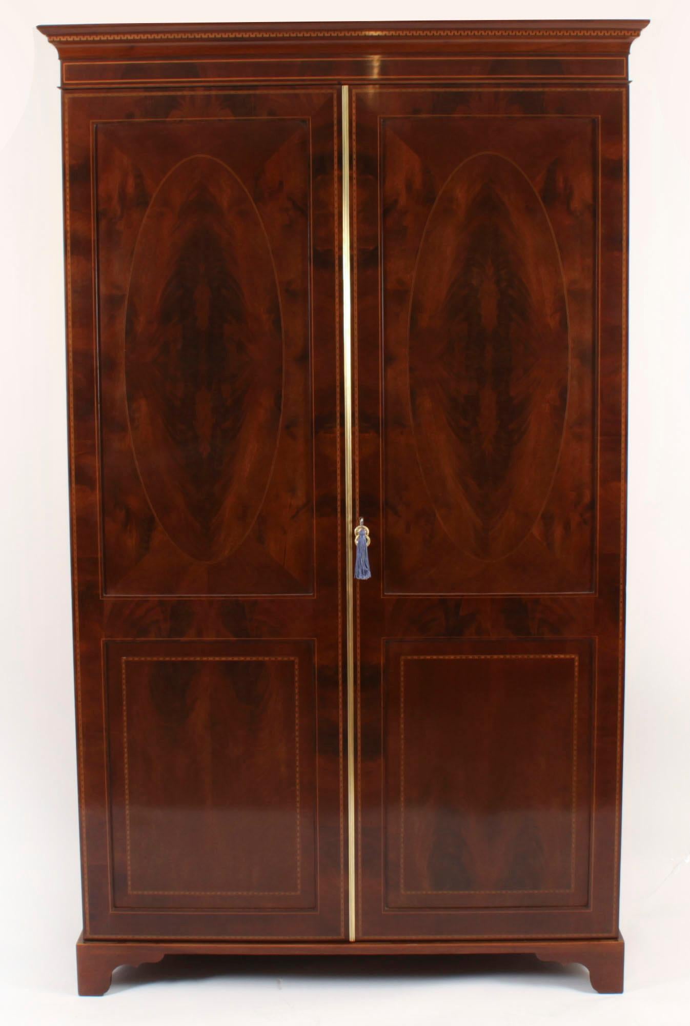 This is an impressive English antique Edwardian Sheraton Revival flame mahogany inlaid wardrobe, late 19th century in date.

It has a moulded cornice with a crossbanded frieze over two panel doors with oval quarter veneered panels decorated with