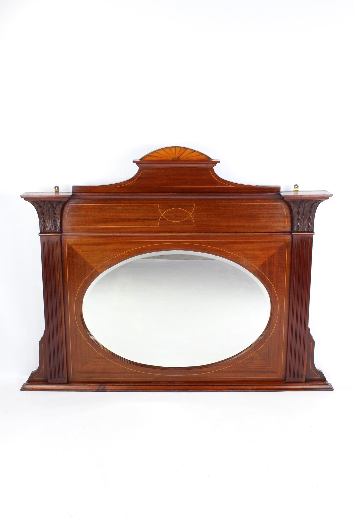 A handsome large antique Edwardian mahogany and inlaid framed overmantle mirror dating from circa 1905. With an oval bevelled mirror plate flanked by moulded pilasters with acanthus carved capitals. In a mahogany veneer, beautifully figured with