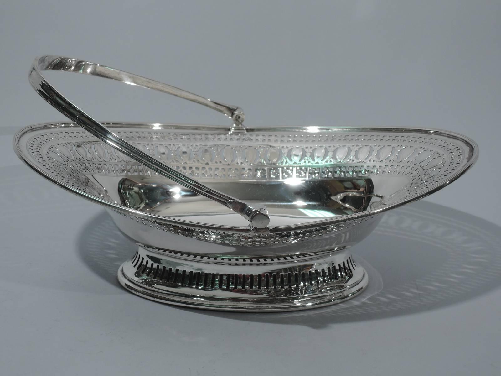 Edwardian neoclassical sterling silver basket. Made by Walker & Hall in Sheffield in 1902. Ovoid with tapering sides and flared rim. Rests on raised ovoid foot. Tapering swing handle. Solid well bordered by pierced and engraved ornament. Foot has