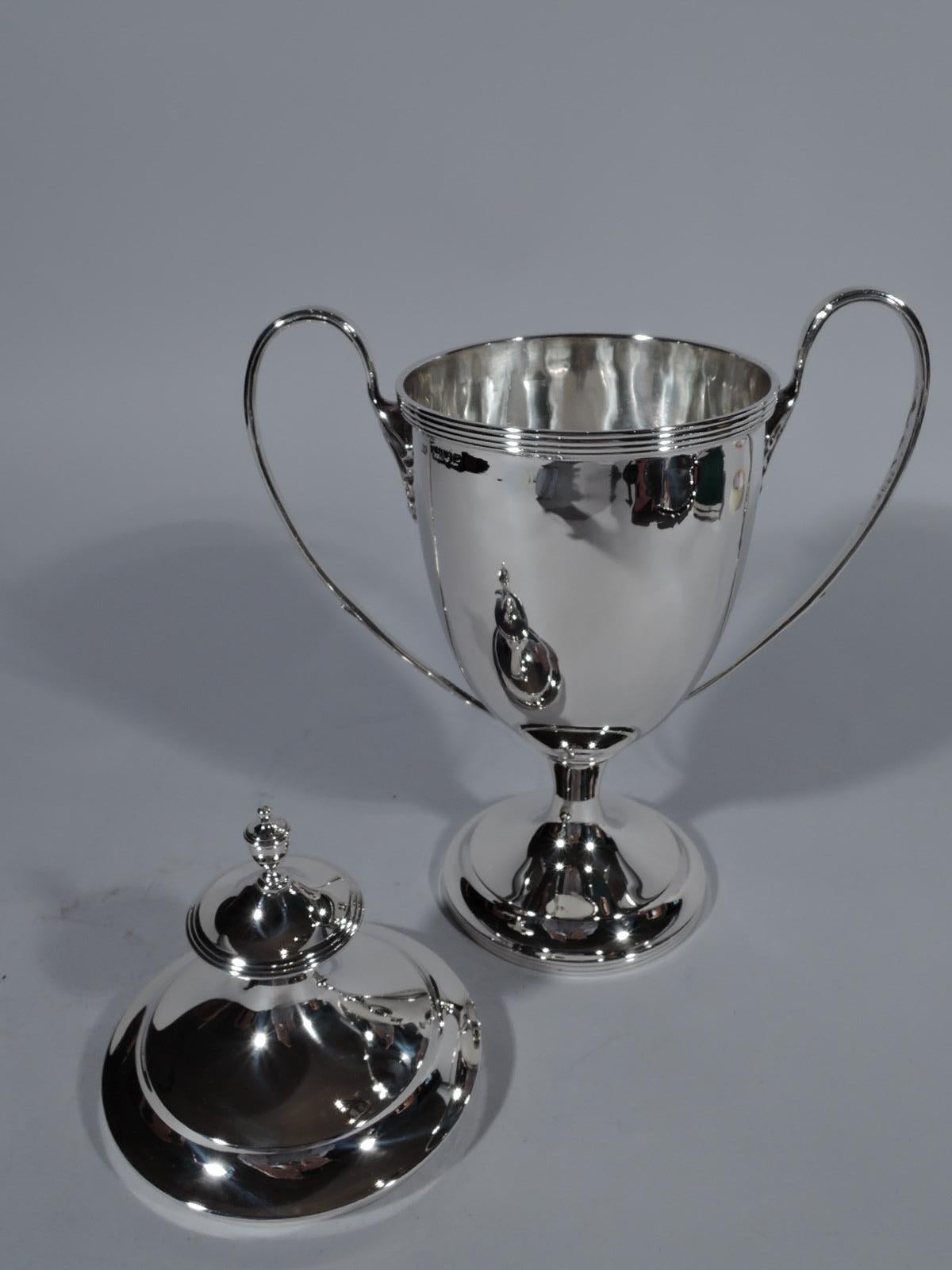 Edwardian neoclassical sterling silver trophy cup. Made by Lionel Alfred Crichton in London in 1910. Elegant amphora vase with oval bowl on spool stem flowing into raised round foot. High-looping side handles with leaf mounts. Cover double domed