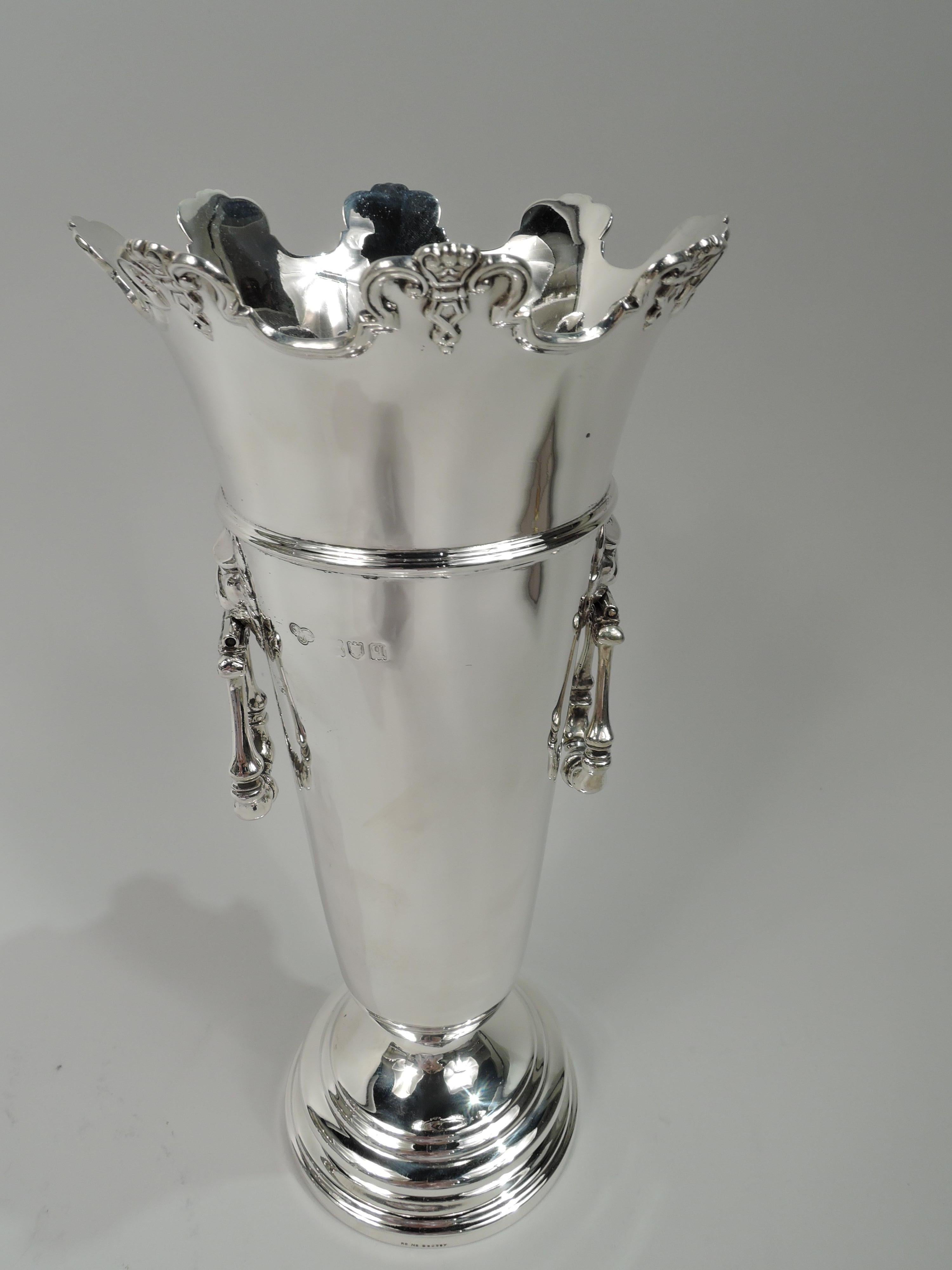George V sterling silver vase. Made by Goldsmiths & Silversmiths Co. Ltd in London in 1911. Tapering and girdled tube on stepped foot. Flared and castellated rim with applied molding and ornament. Lion’s head side mounts with hinged and turned
