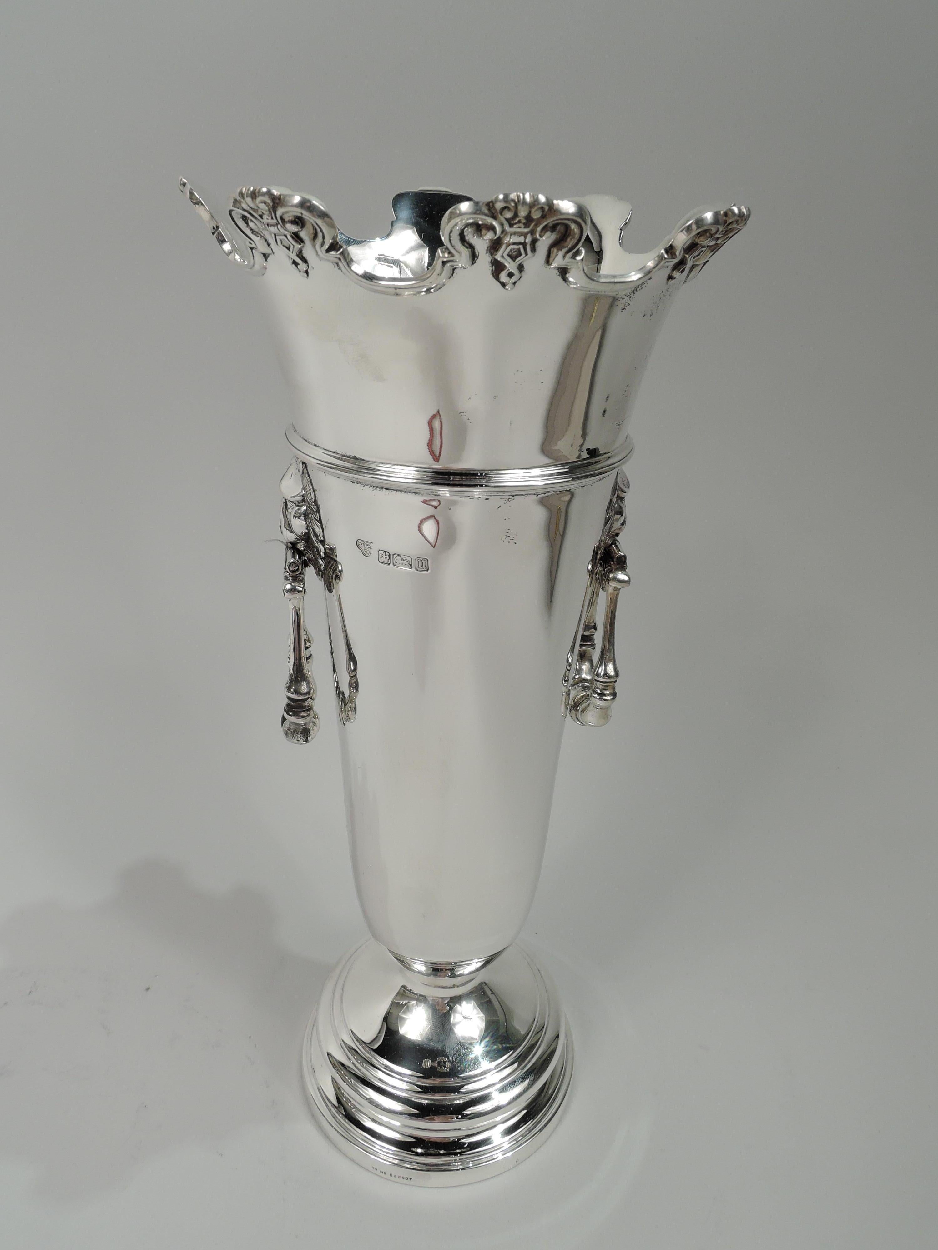 George V sterling silver vase. Made by Goldsmiths & Silversmiths Co. Ltd in Sheffield in 1912. Tapering and girdled tube on stepped foot. Flared and castellated rim with applied molding and ornament. Lion’s head side mounts with hinged and turned