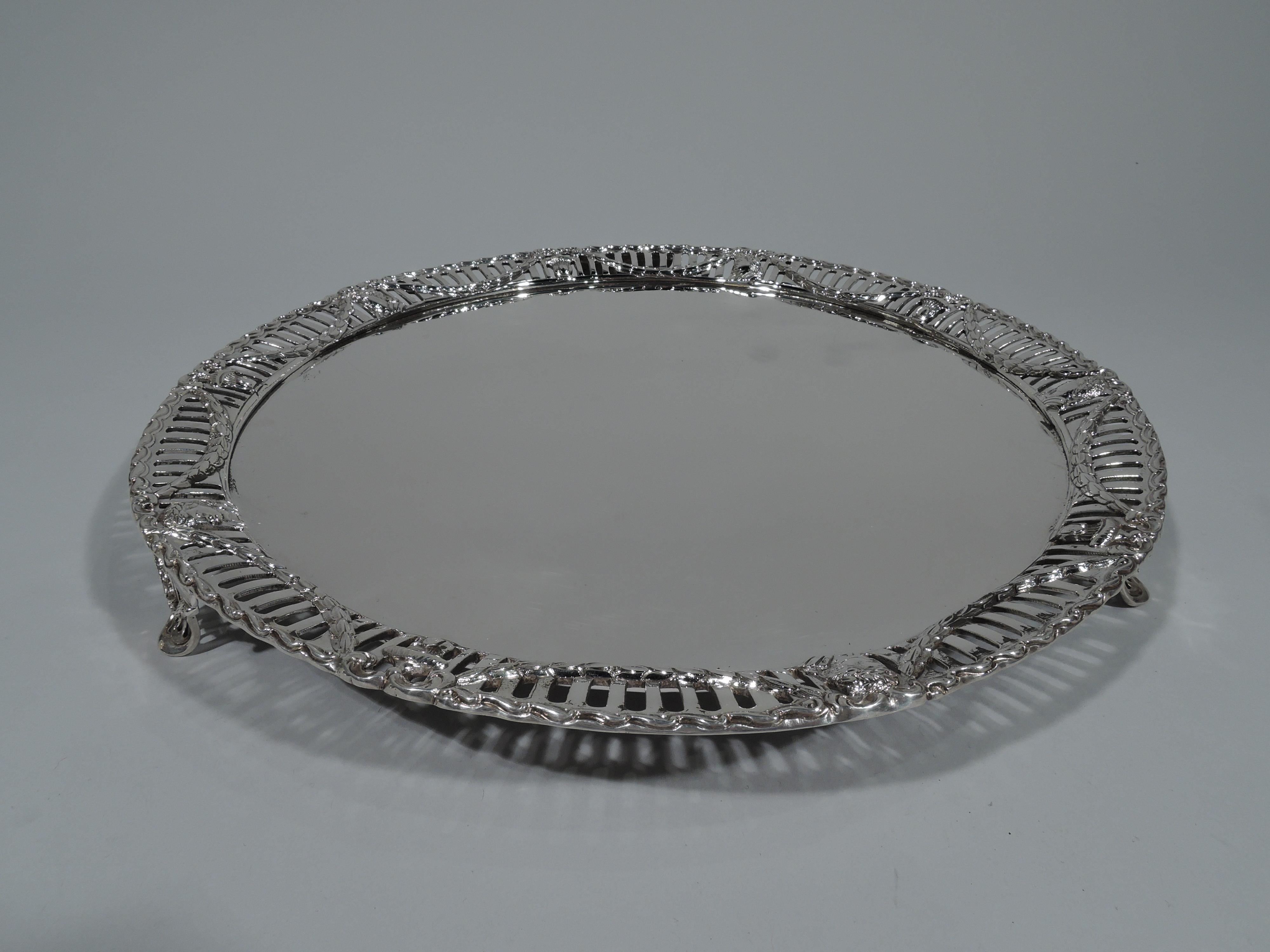 Edwardian sterling silver salver. Made by Charles Stuart Harris & Sons in London in 1908. Round with solid well. Tapering and pierced shoulder with applied swags, vases, and laurel-wreathed heads. Rim has applied Vitruvian scrollwork. Four supports