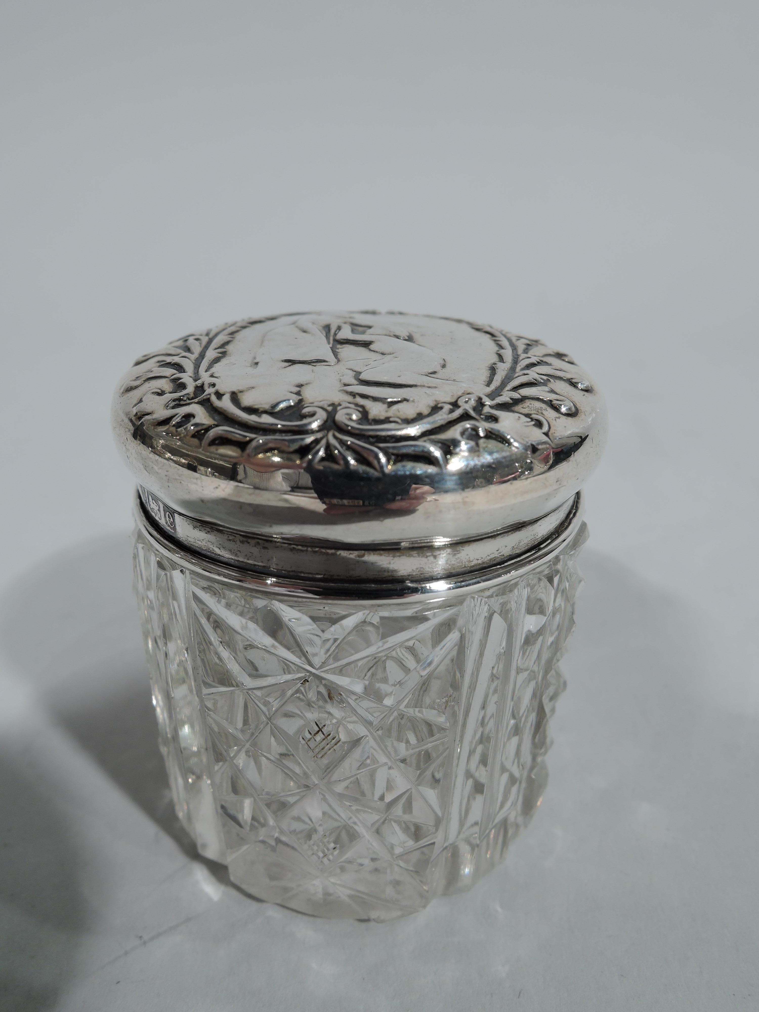 Edwardian cut-glass powder jar with sterling silver cover. Made by Adie Bros in Birmingham in 1904. Drum form with diaper ornament alternating with double flutes. On cover are two figures of which one kneeling in leafy scroll wreath. Cover fully