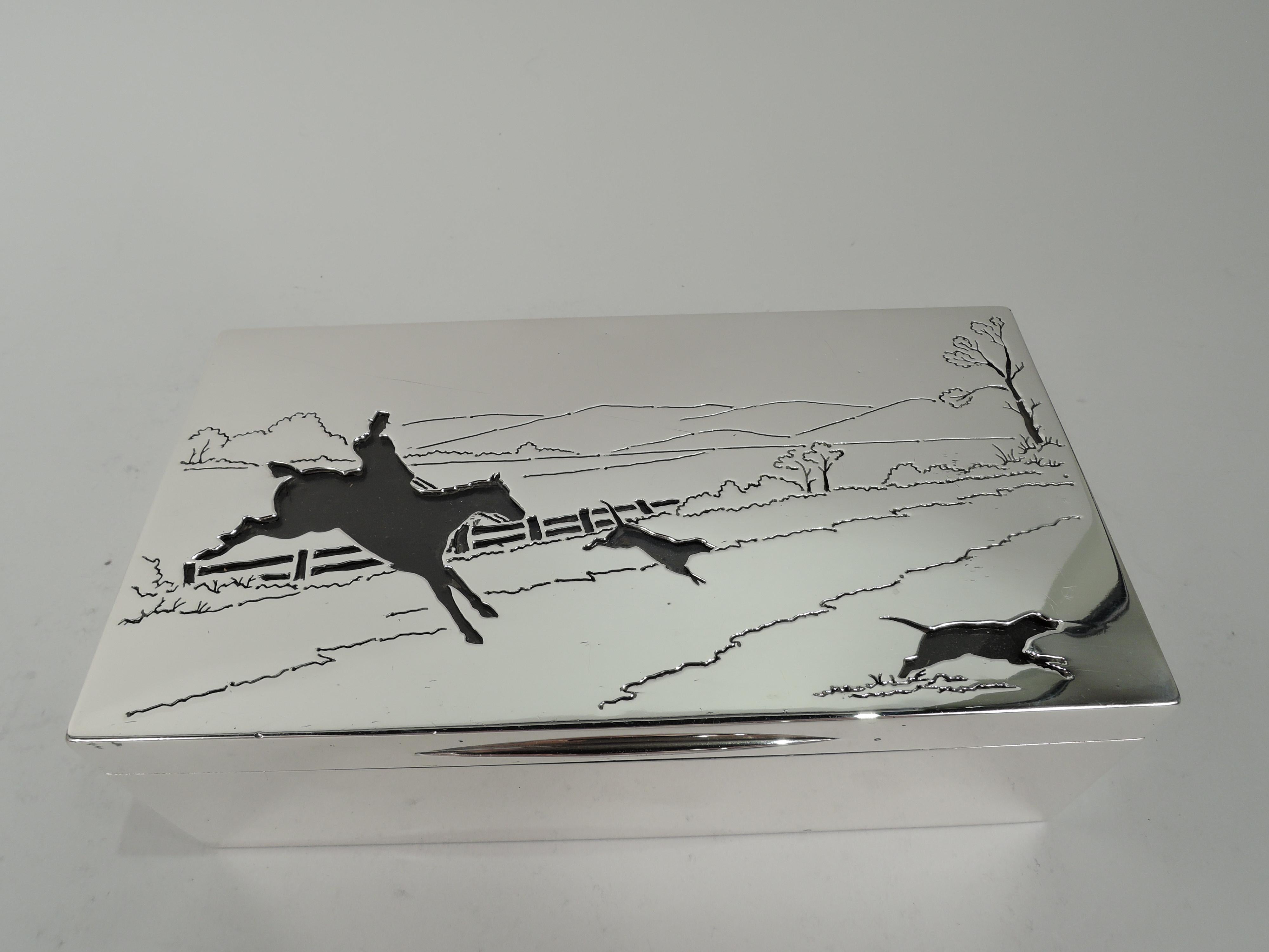 Edwardian sterling silver box. Made by Goldsmiths & Silversmiths Co. Ltd in London in 1910. Rectangular with straight sides. Cover hinged and flat with tapering tab. On cover top is hunting scene. In foreground a horse takes a fence the hounds