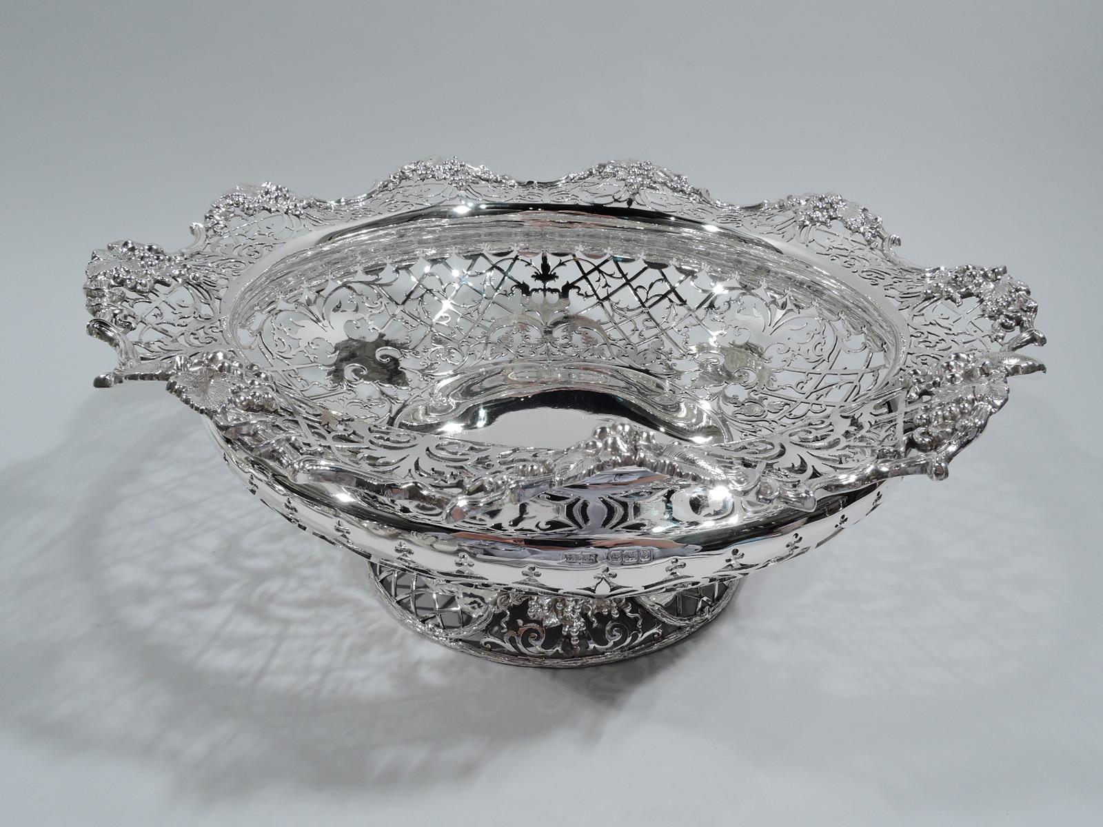 George V sterling silver bowl. Made by James Dixon & Sons in Sheffield in 1917. Bellied with round shaped solid well, wavy rim, and domed foot. Open diaper and scrollwork with tendrils, and solid scrolled and foliate frames (vacant). Bowl and foot