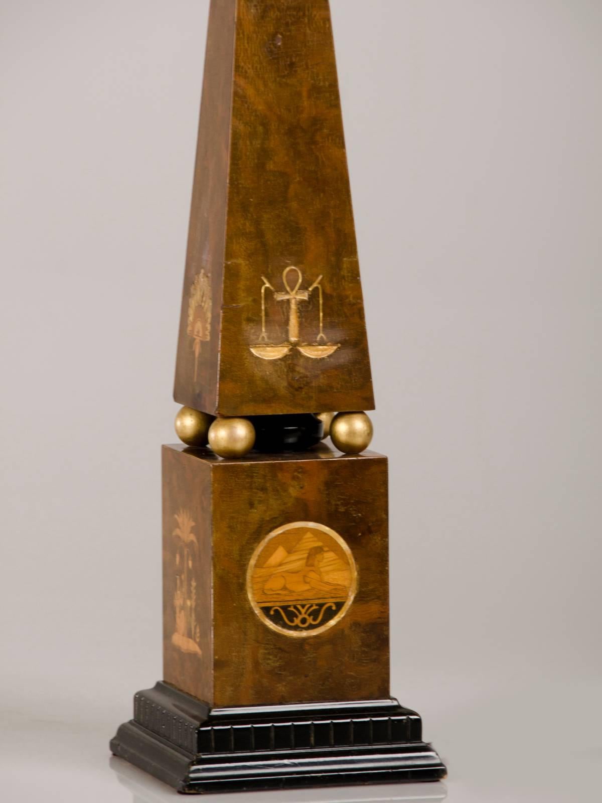 This smashing antique English Egyptian Revival table lamp, circa 1910, features a plinth base supporting an obelisk with four gilded spheres in between the base and column. Please enlarge and zoom on the photographs to see the wonderful marquetry