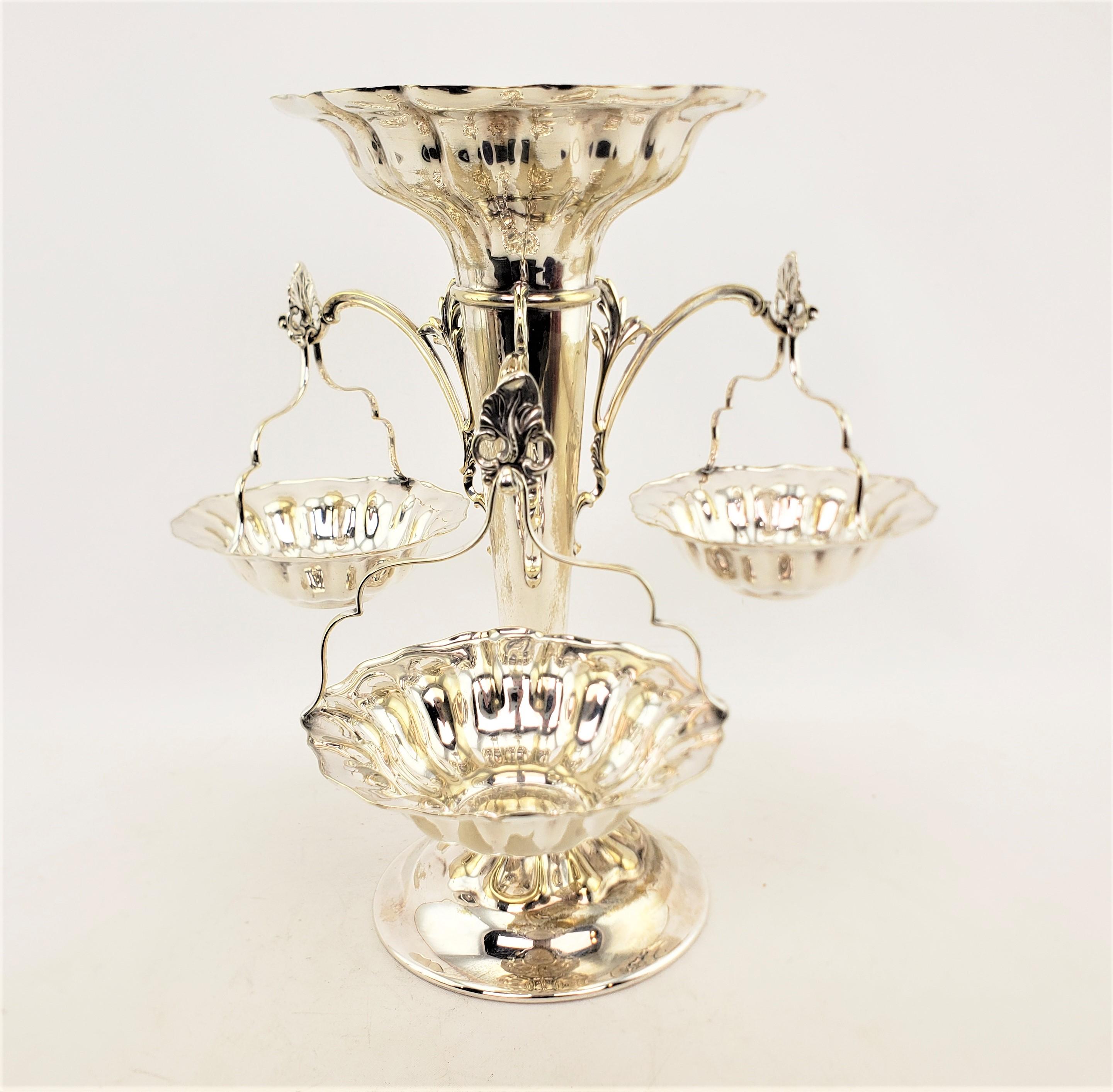 This antique silver plated epergne was made by the Elkington Plate Co. of England, and dating to approximately 1920 and done in a Victorian style. The epergne or centerpiece is made with a central trumpet vase with a scalloped base, and three