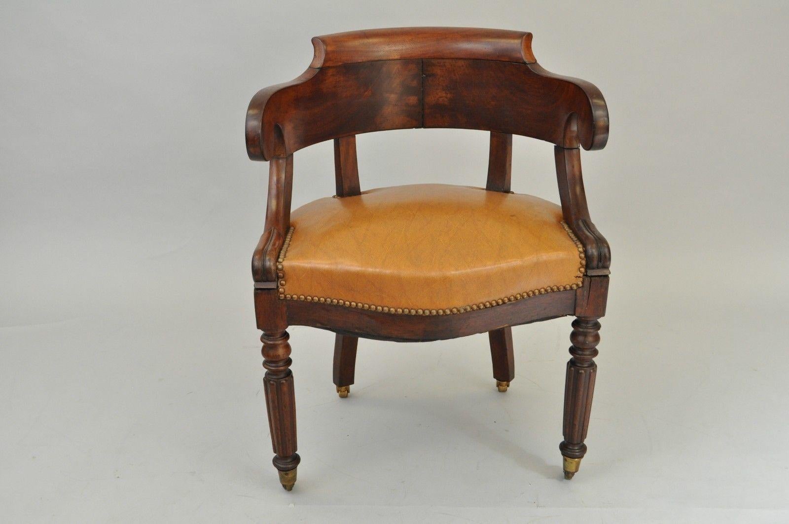 Antique English Empire or Regency period mahogany library chair. Item features solid carved mahogany frame, scrolled arms and curved back, caramel leather upholstery, Brass rolling casters, classical period form circa 1800s, period. Measurements:
