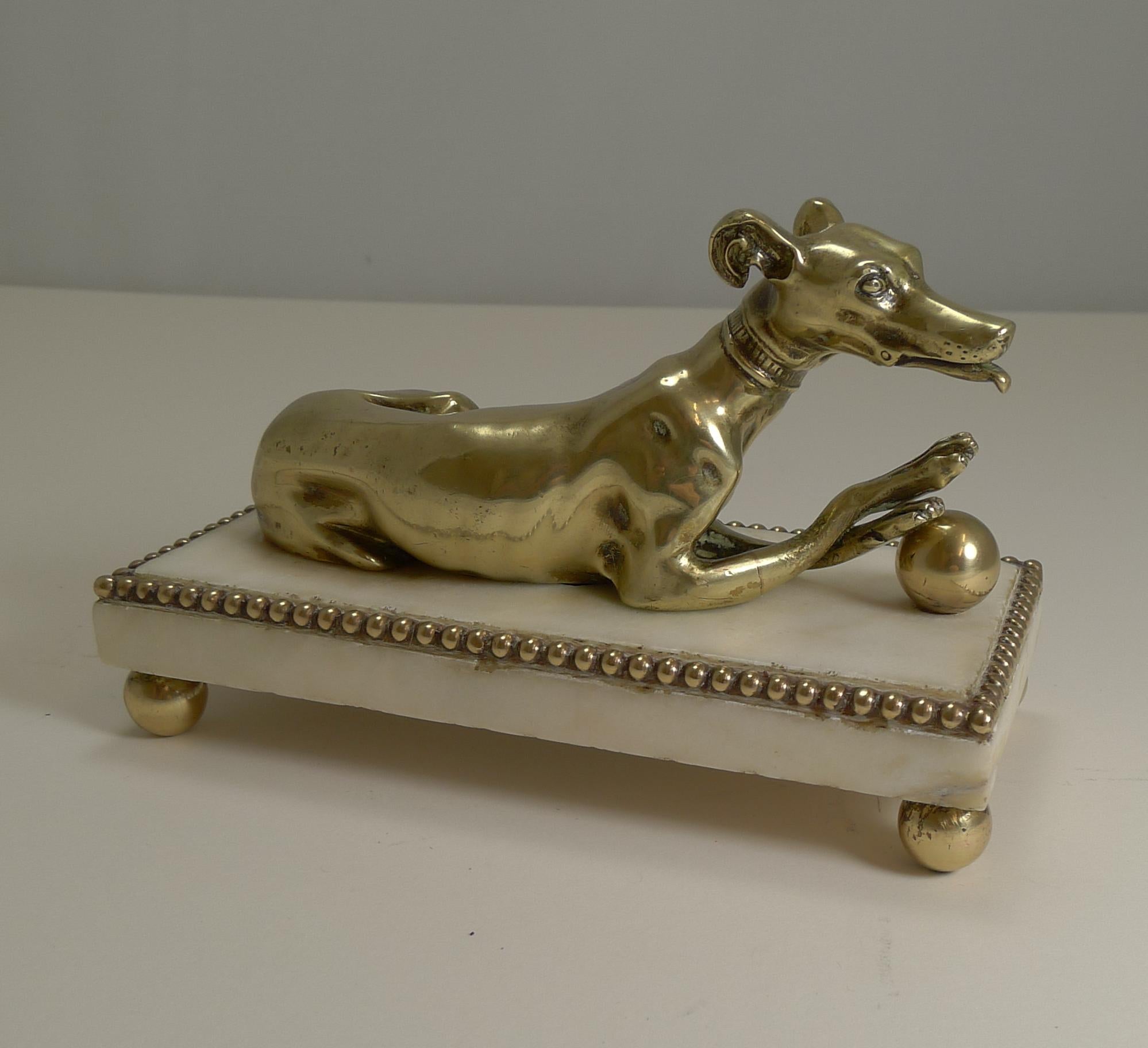 A wonderful and most unusual desk-top accessory, a novelty paper or note clip in the from of a very handsome Greyhound.

Figured in cast English brass, the dog has his crossed paws on a ball and has detail such as collar with loose movable leash