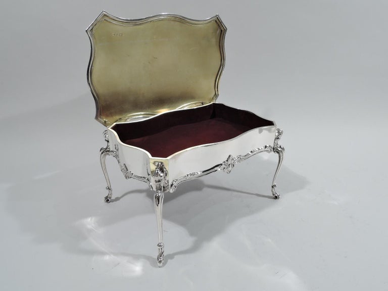 Edwardian sterling silver jewelry box. Made by William Comyns in London in 1902. In form of Rococo table: Serpentine with cantered corners and four volute-scroll mounted and leaf-capped legs. Cover hinged with engraved armorial. Box interior lined