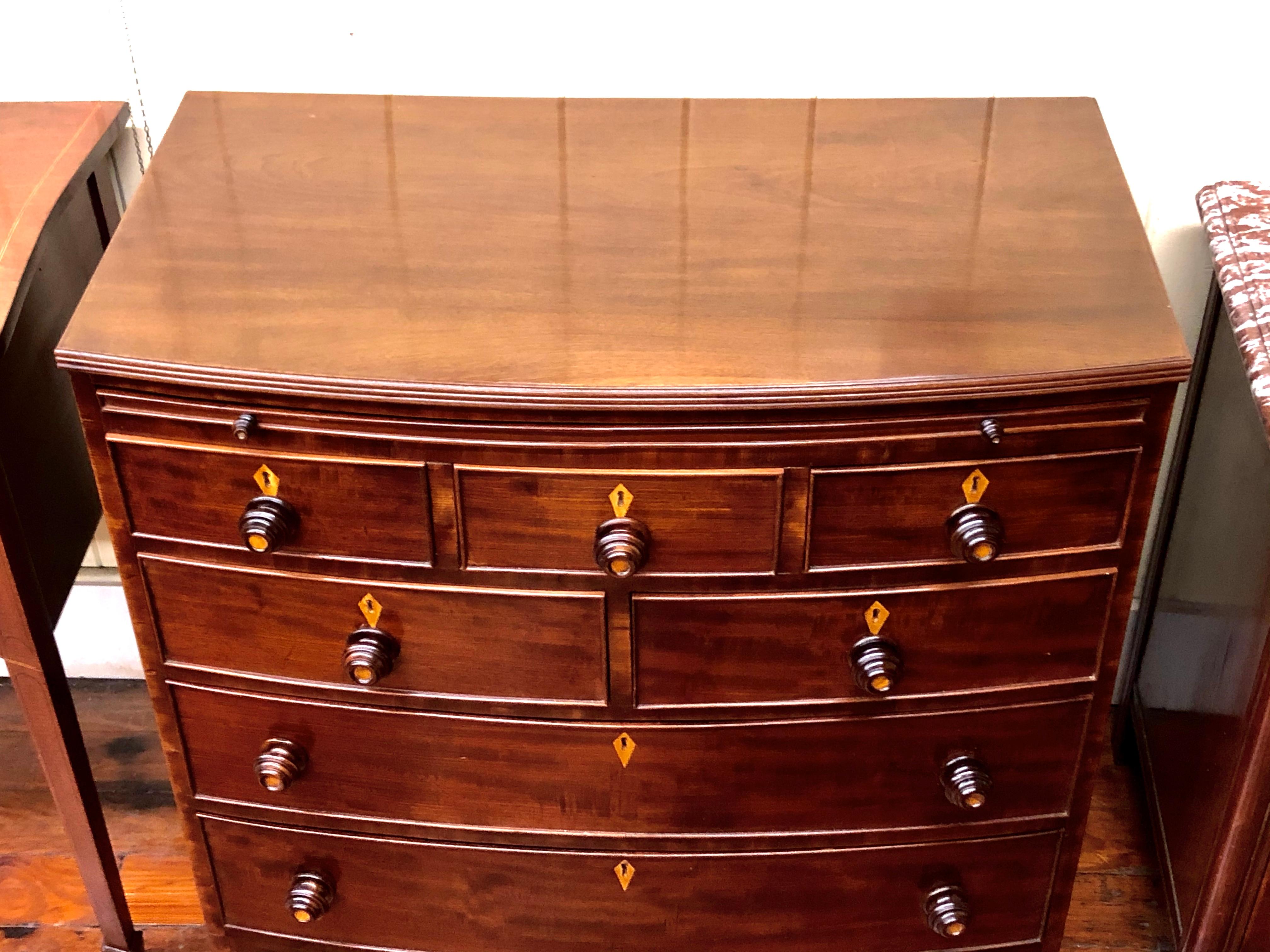 Extraordinary Antique English highly figured bowfront Chest of Drawers with exceptional antique inlaid mahogany round wooden knobs (satinwood inlay in the center). Also has handsome inlaid diamond-shape escutcheons. The chest has a rare pull-out
