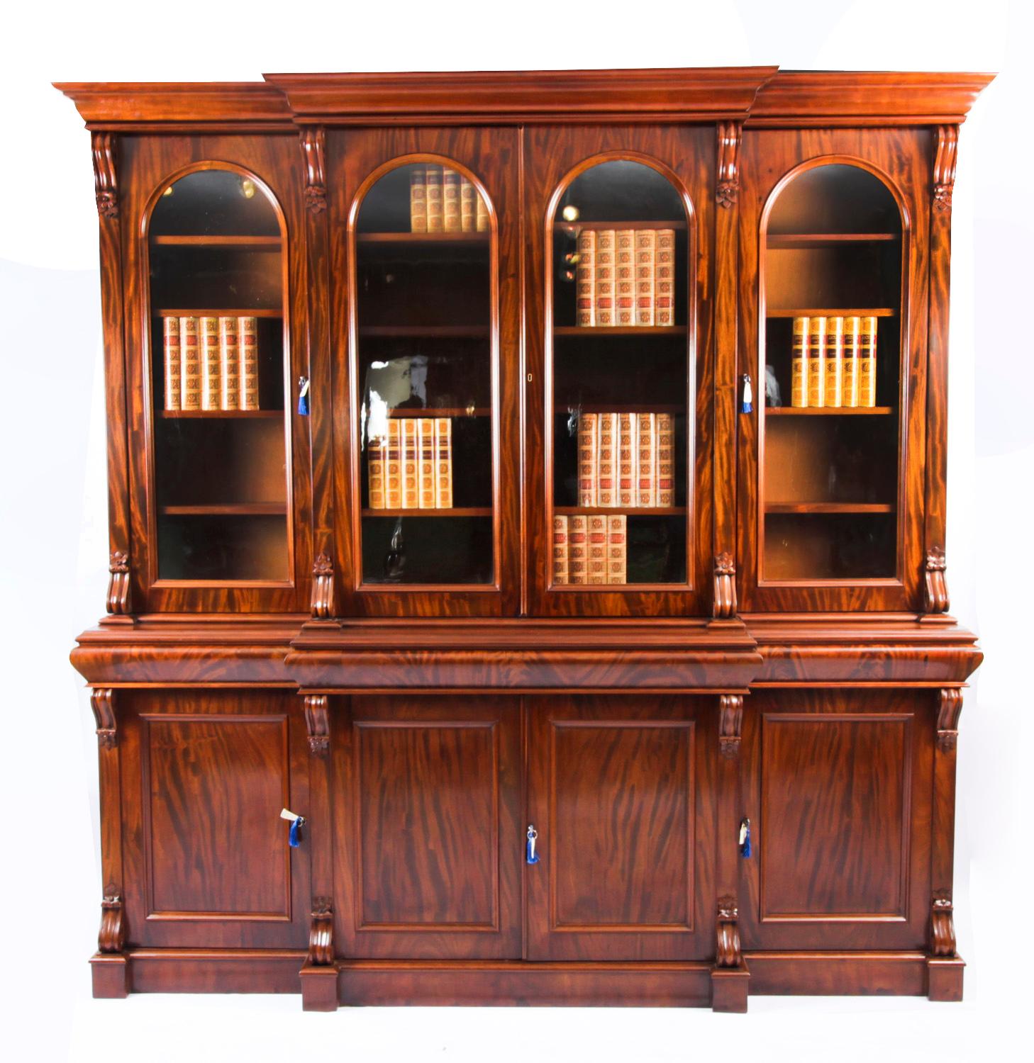 This is a beautiful antique Victorian flame mahogany four door library breakfront bookcase, masterfully crafted in rich solid mahogany, Circa 1860 in date.

This magnificent bookcase features four arched top glazed doors in the upper section