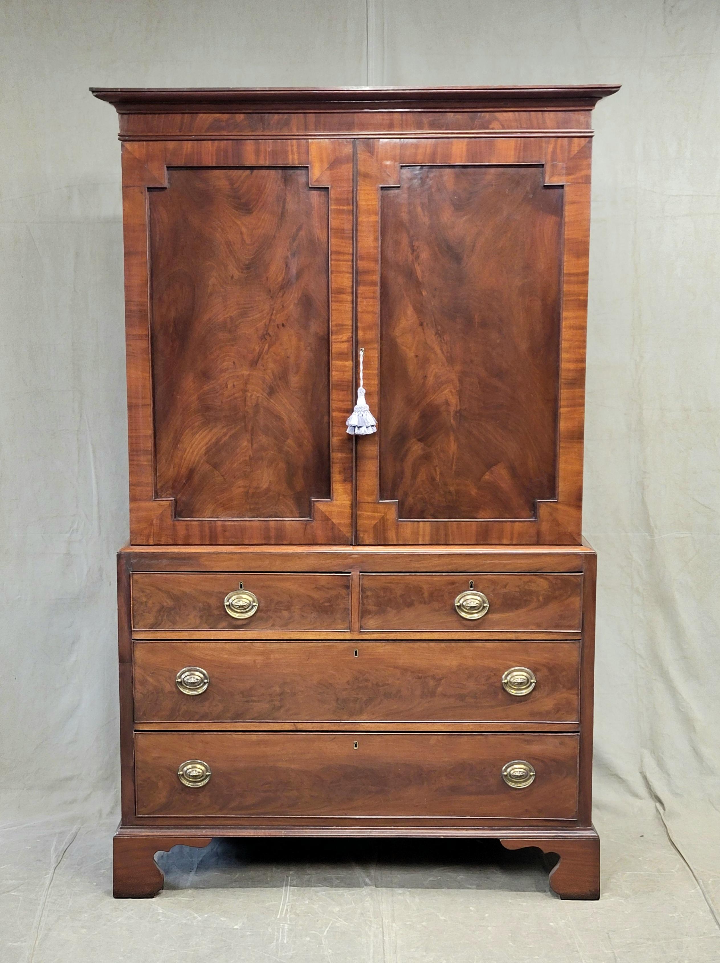 An absolutely gorgeous antique English flame mahogany linen press with oval brass pulls sits a top stunning bracket feet. Crafted in the late 1800s primarily out of solid and mahogany veneers with the exception being pine comprising the drawer