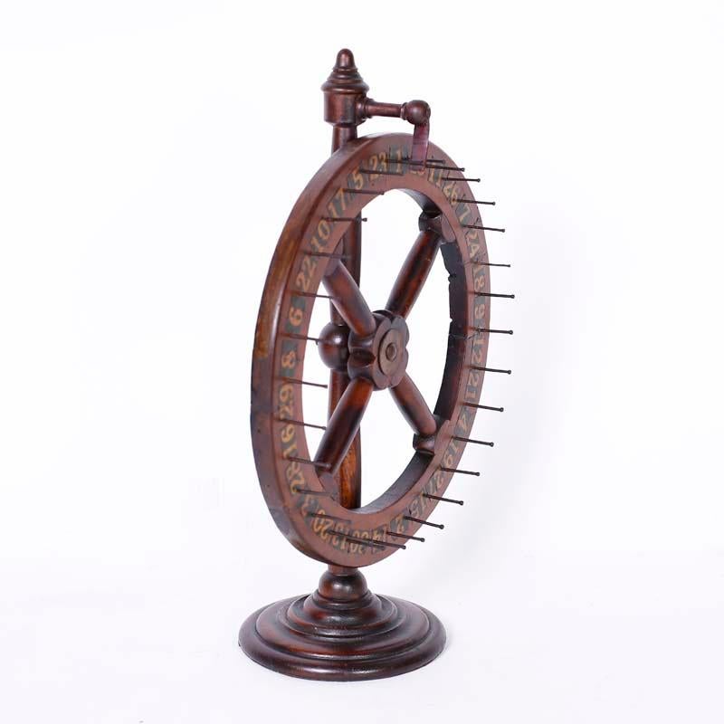 Une roue de jeu anglaise antique et transportable, fabriquée en pin foncé par une gomme-laque vieillie, avec un bouchon en cuir et des numéros découpés de 1 à 30, et posée sur une base ronde classique. Faites vos jeux.