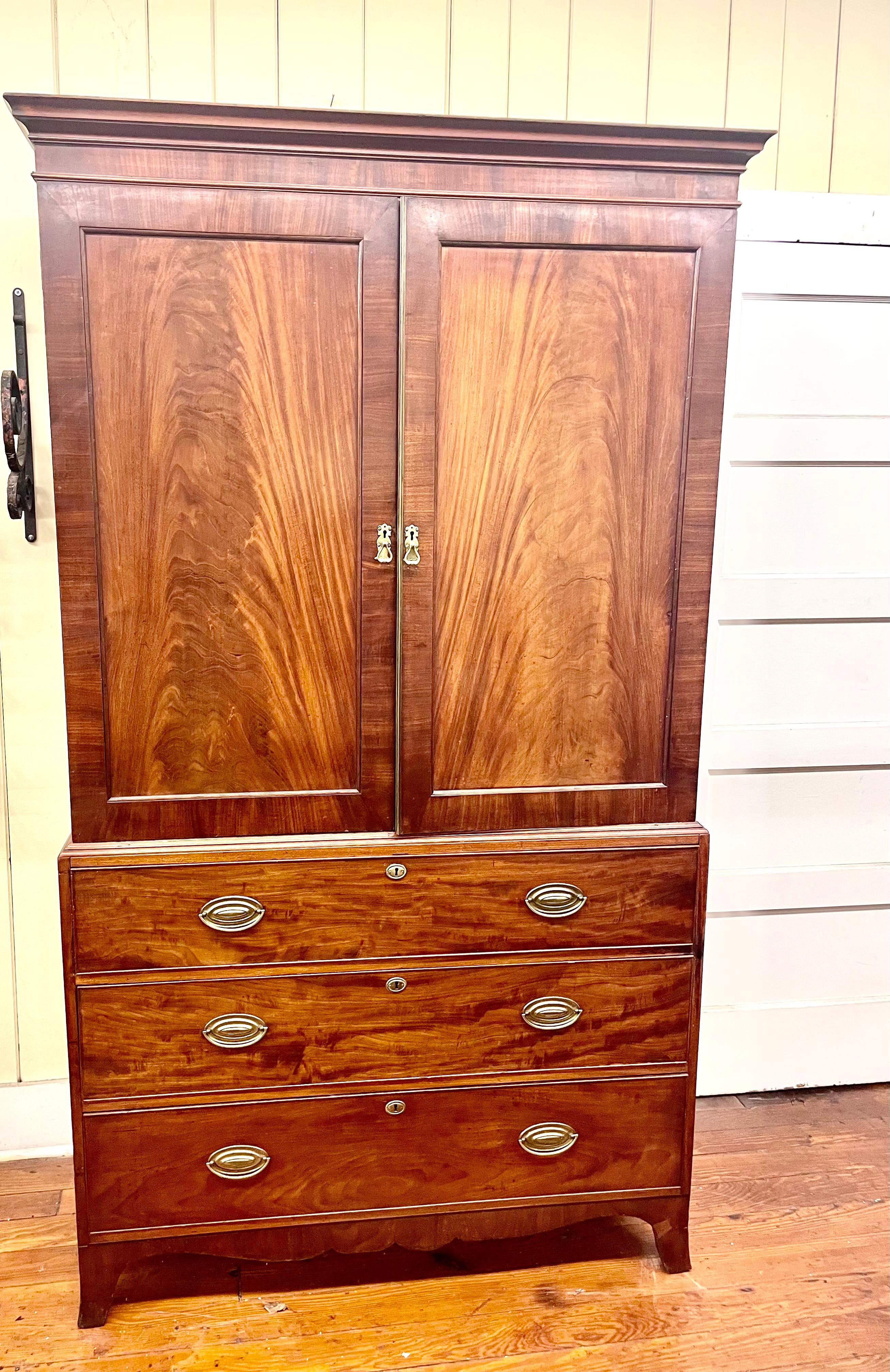 Superb quality antique English bookmatched figured mahogany Hepplewhite style linen press which retains its original interior sliding linen trays. The panelled doors are inset with gorgeous bookmatched crotch mahogany. This Linen Press is original