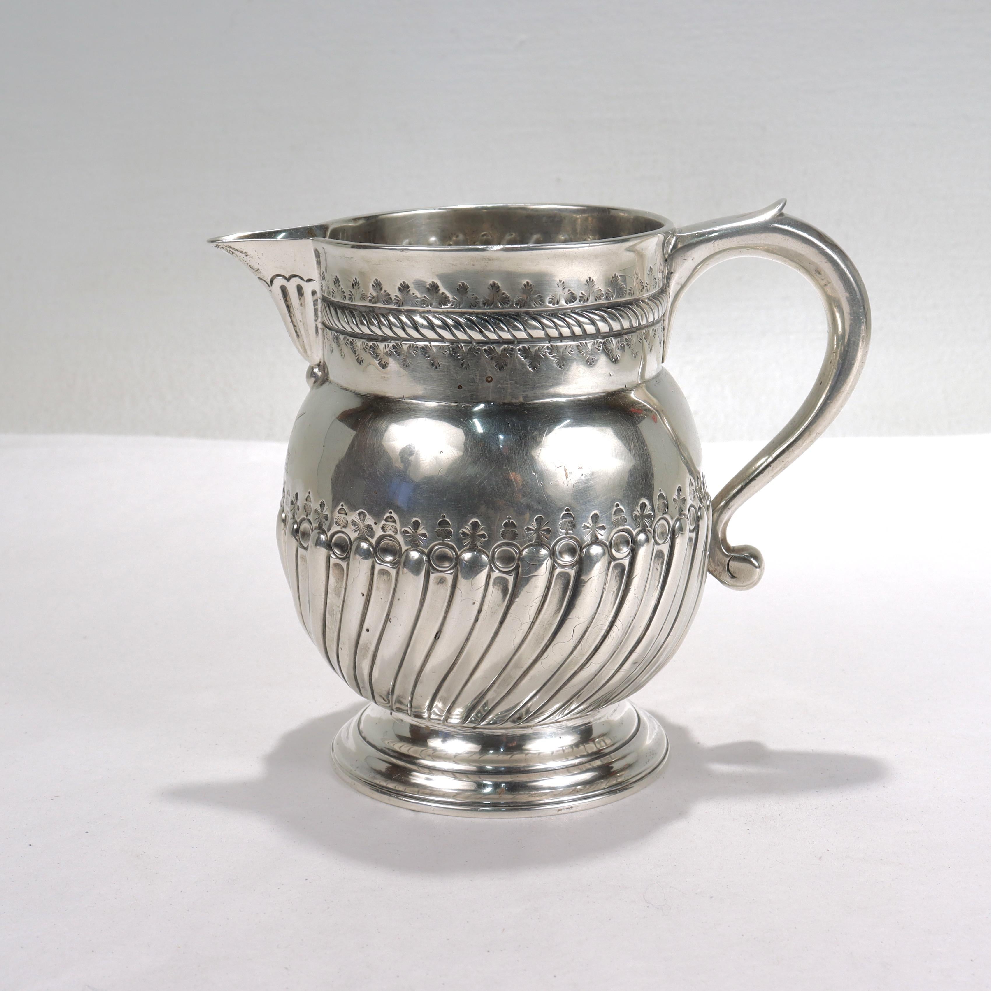 A fine antique, early 18th century English silver milk jug.

In Britannia silver.

Made by Nathaniel Gulliver.

The jug having punch-work decoration of repeating trefoil leaves to the top and alternating acorns & starbursts above a gadrooned