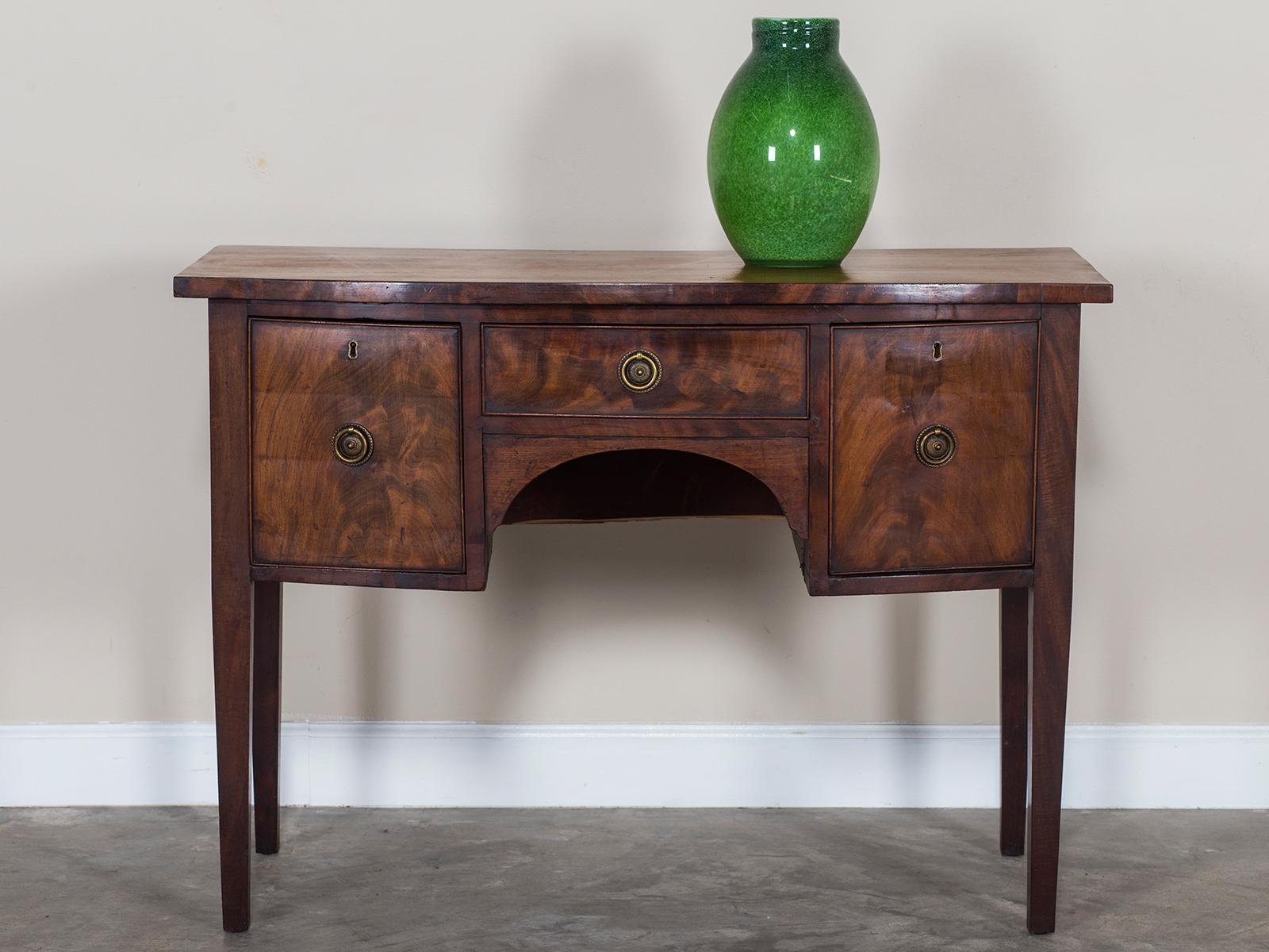 The simplicity of this antique English George III period bow front sideboard table circa 1820 gives it a certain modern quality. Please enlarge and zoom on the additional photographs to see the superb quality of the mahogany used on this antique