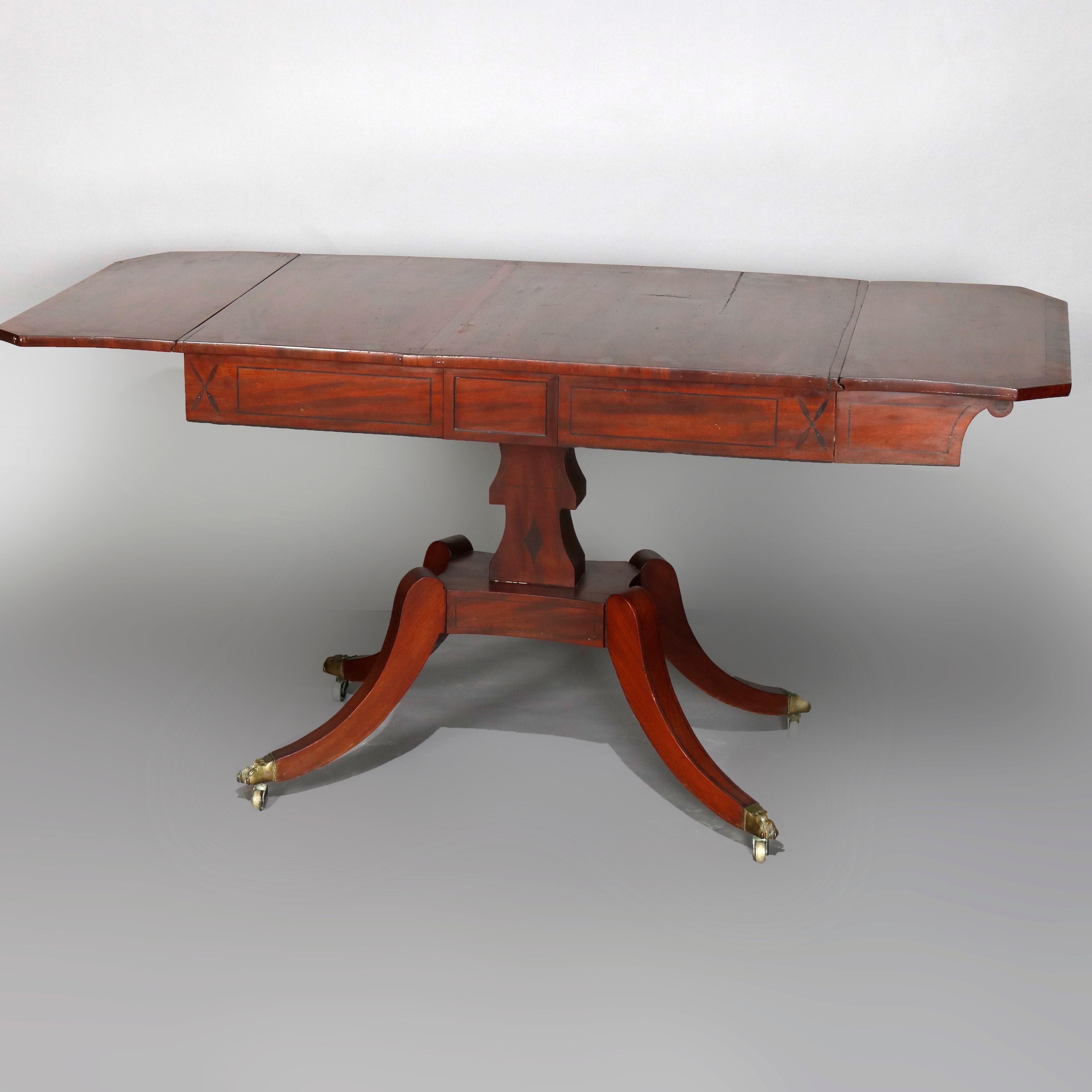 An antique English George III table offers deeply striated mahogany construction with top having crossbanding over two drawers and drop leaves raised on pedestal with four concave form legs terminating in bronze paw form caps, circa
