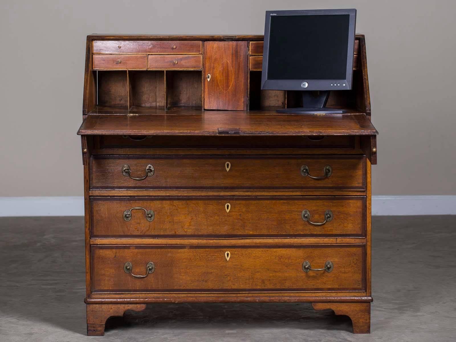 An antique English Georgian oak crossbanded with mahogany drop front secretary bureau chest desk from England, circa 1800 having a slant front supported by lopers. This handsome George III period oak desk has a beautiful patina from years of waxing