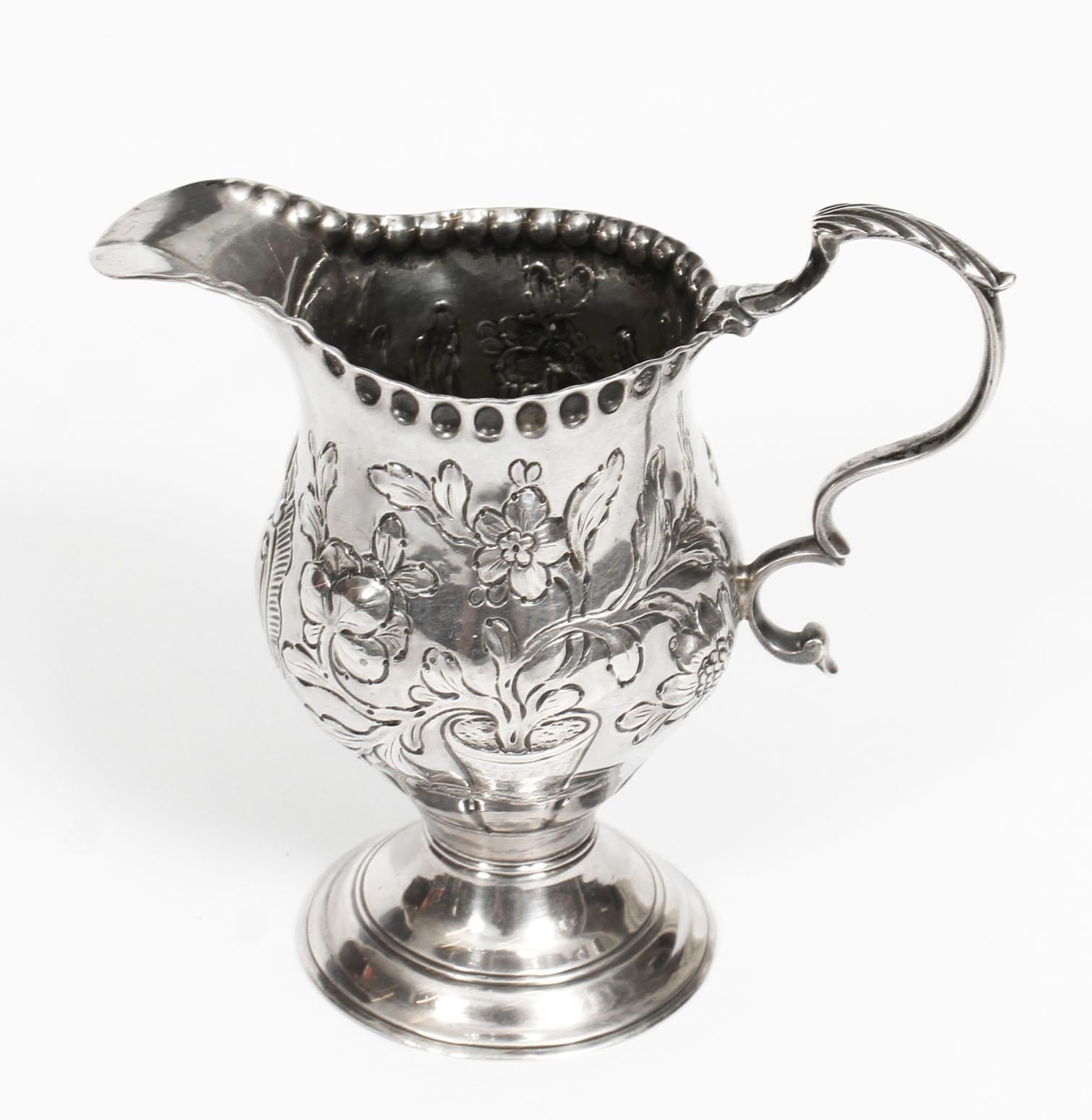 This is a wonderful English antique George III sterling silver cream jug with hallmarks for London 1770.

The beautiful helmet shaped jug is further decorated with embossed tubs of flowers. The blank central cartouche is ready for your own