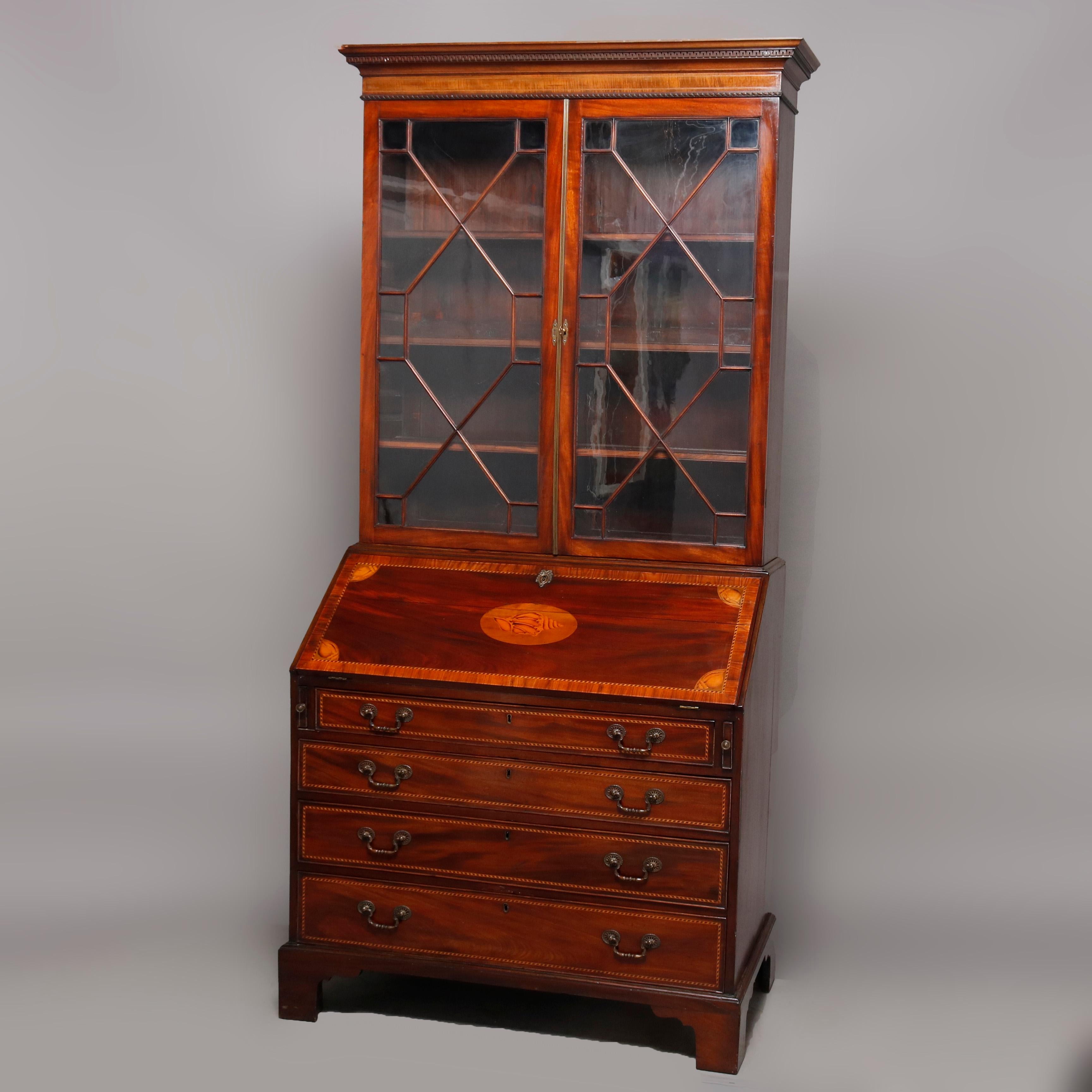 An antique English George III secretary offers flame mahogany construction with upper bookcase having double glass doors with muntins in diamond pattern and surmounting slant front desk with crossbanded and satinwood inlaid parquetry shell medallion