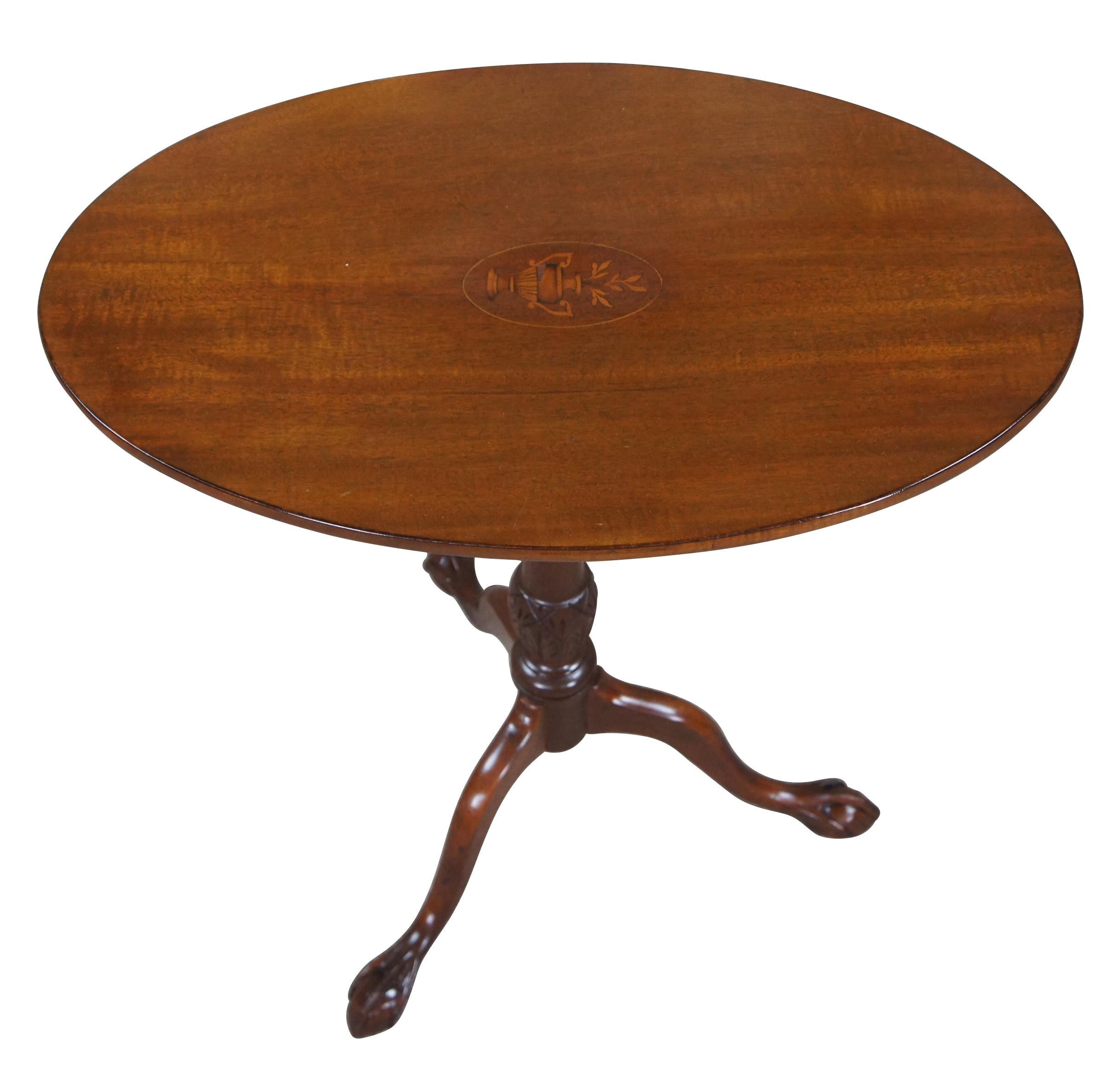 An elegant early 20th century Georgian or Hepplewhite style mahogany tilt-top tea table / candle stand.   Features an oval mahogany tabletop with inlayed neoclassical urn marquetry.  The top is supported by finely carved support, rising over three
