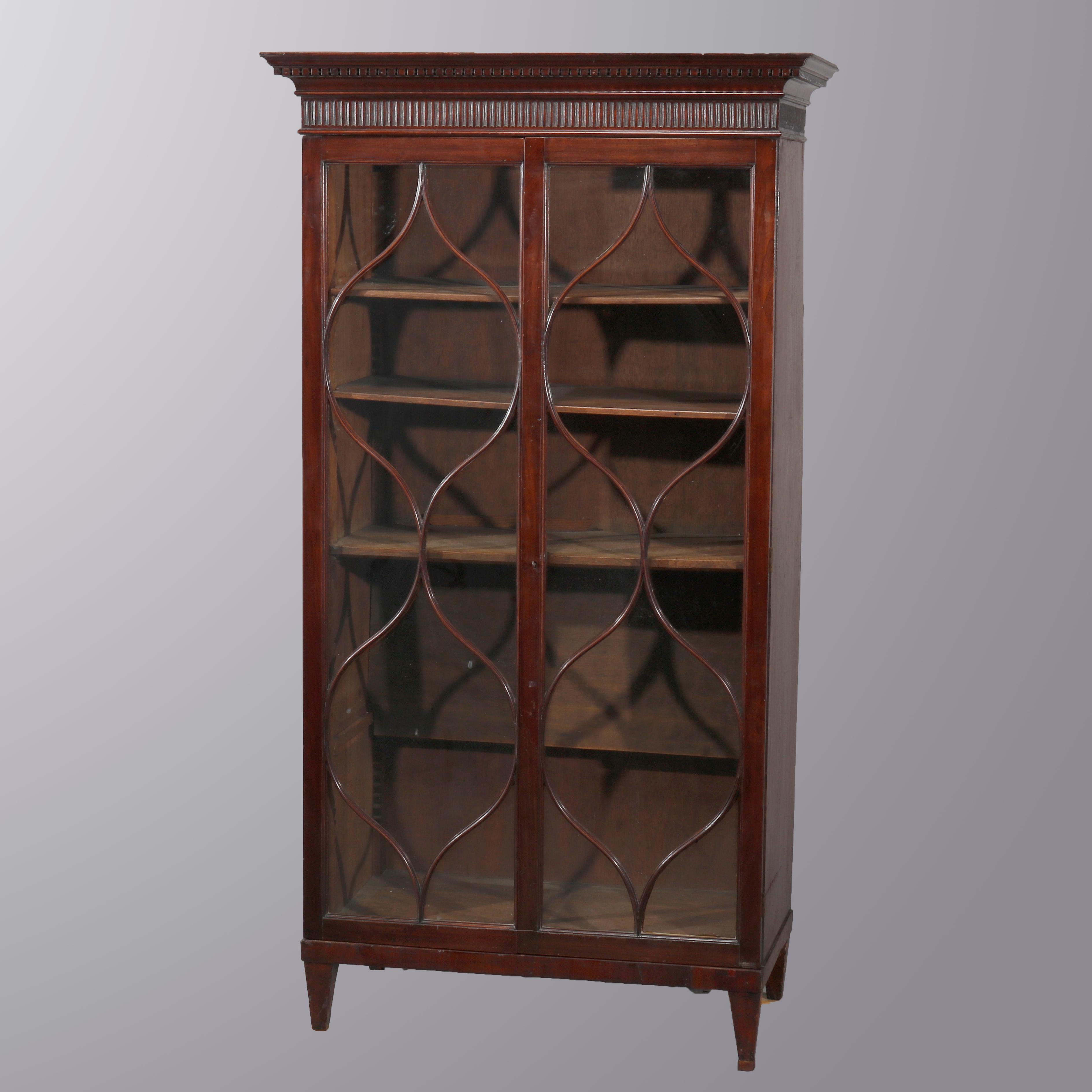 An antique English Georgian bookcase offers mahogany construction with case having reeded frieze over double serpentined mullioned glass doors opening to shelved interior, circa 1810

Measures: 61.5