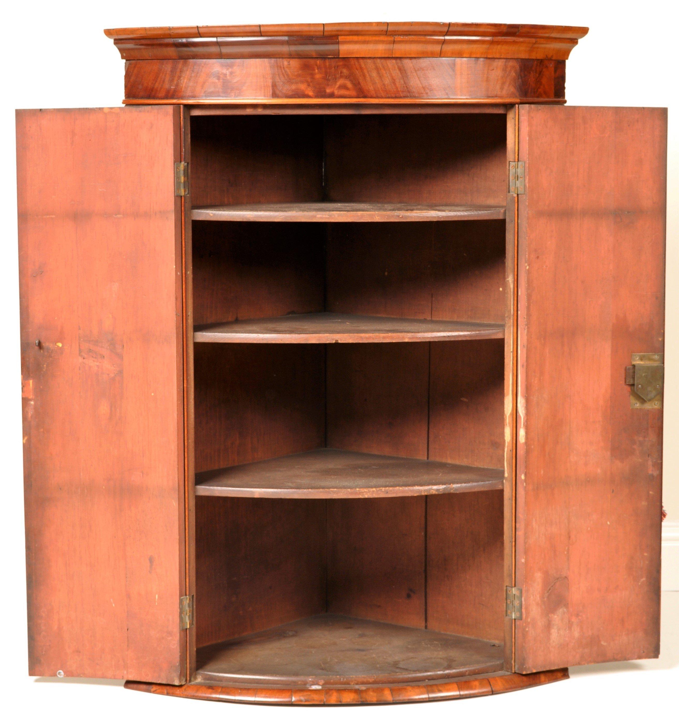 Antique English Georgian flame mahogany bow-fronted corner cabinet, circa 1780. The top with a simple molding below a band of cock beading, having a pair of bowed doors enclosing three shelves, the cabinet retaining the original lock and made from