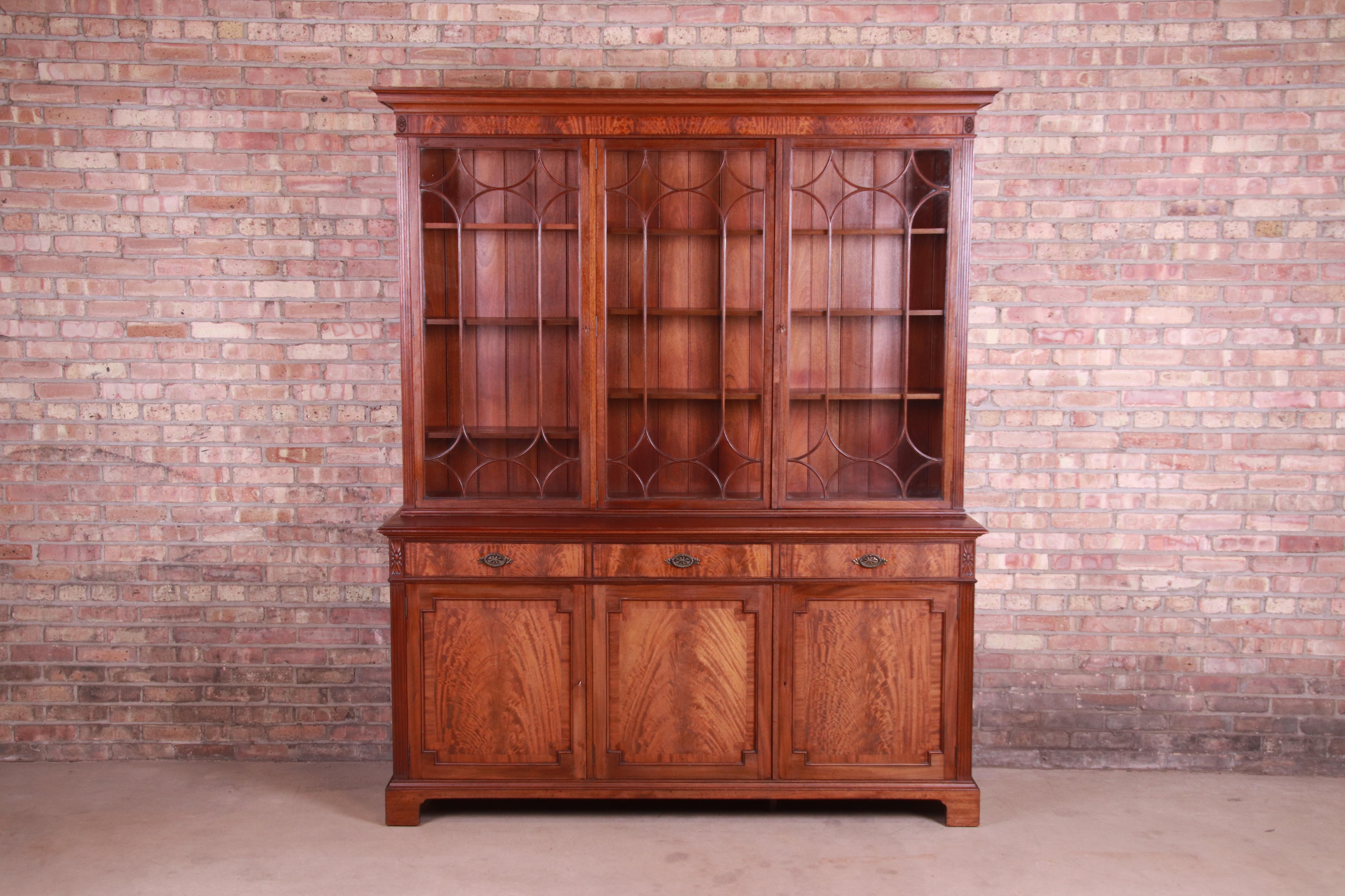 A gorgeous English Georgian breakfront bookcase cabinet

England, late 19th century

Book-matched flame mahogany, with mullioned glass front doors and original brass hardware. Cabinets lock, and key is included.

Measures: 72