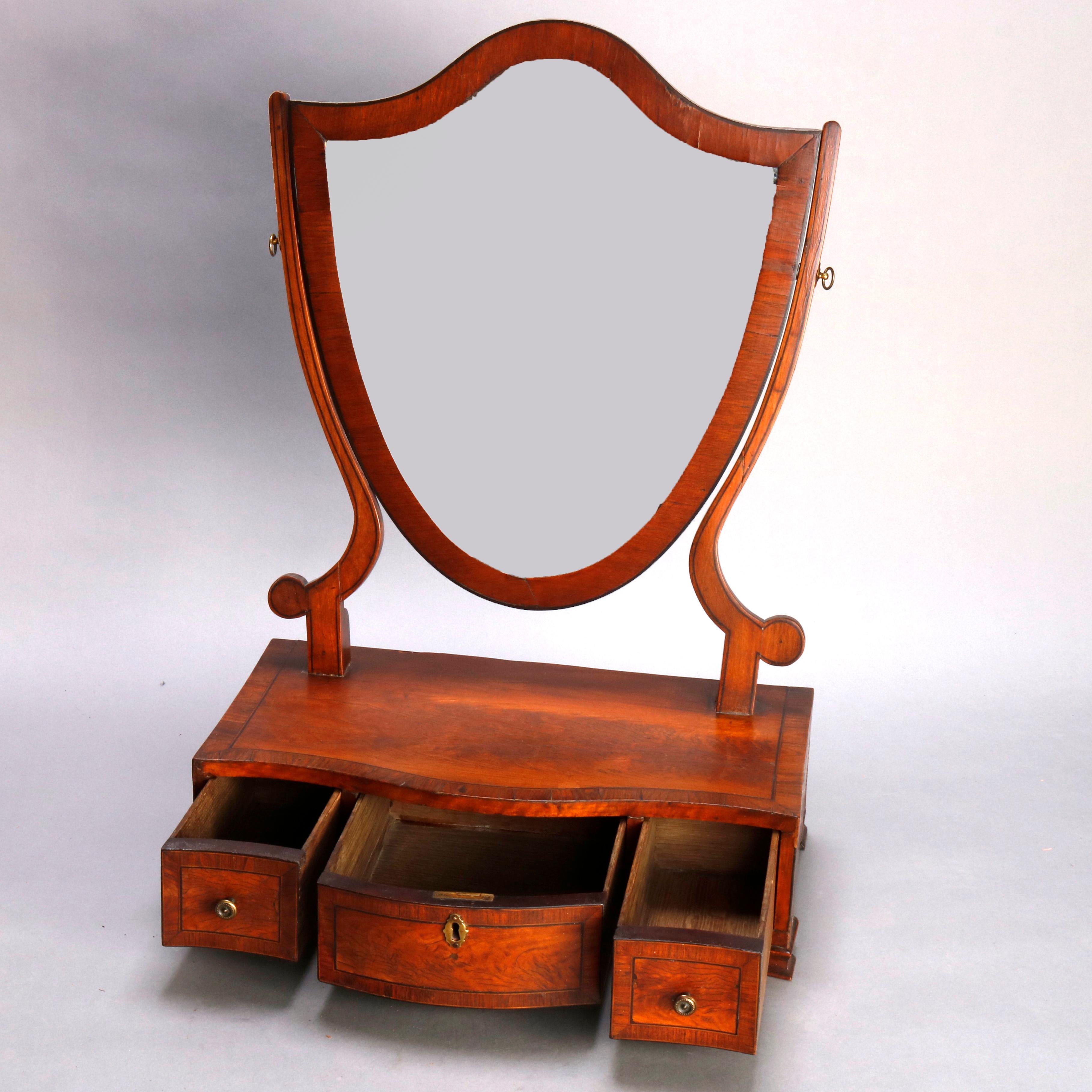An antique English Georgian dresser shaving mirror offers flame mahogany construction with shield form mirror surmounting crossbanded base with three drawers and raised on bracket feet, circa 1810

***DELIVERY NOTICE – Due to COVID-19 we are