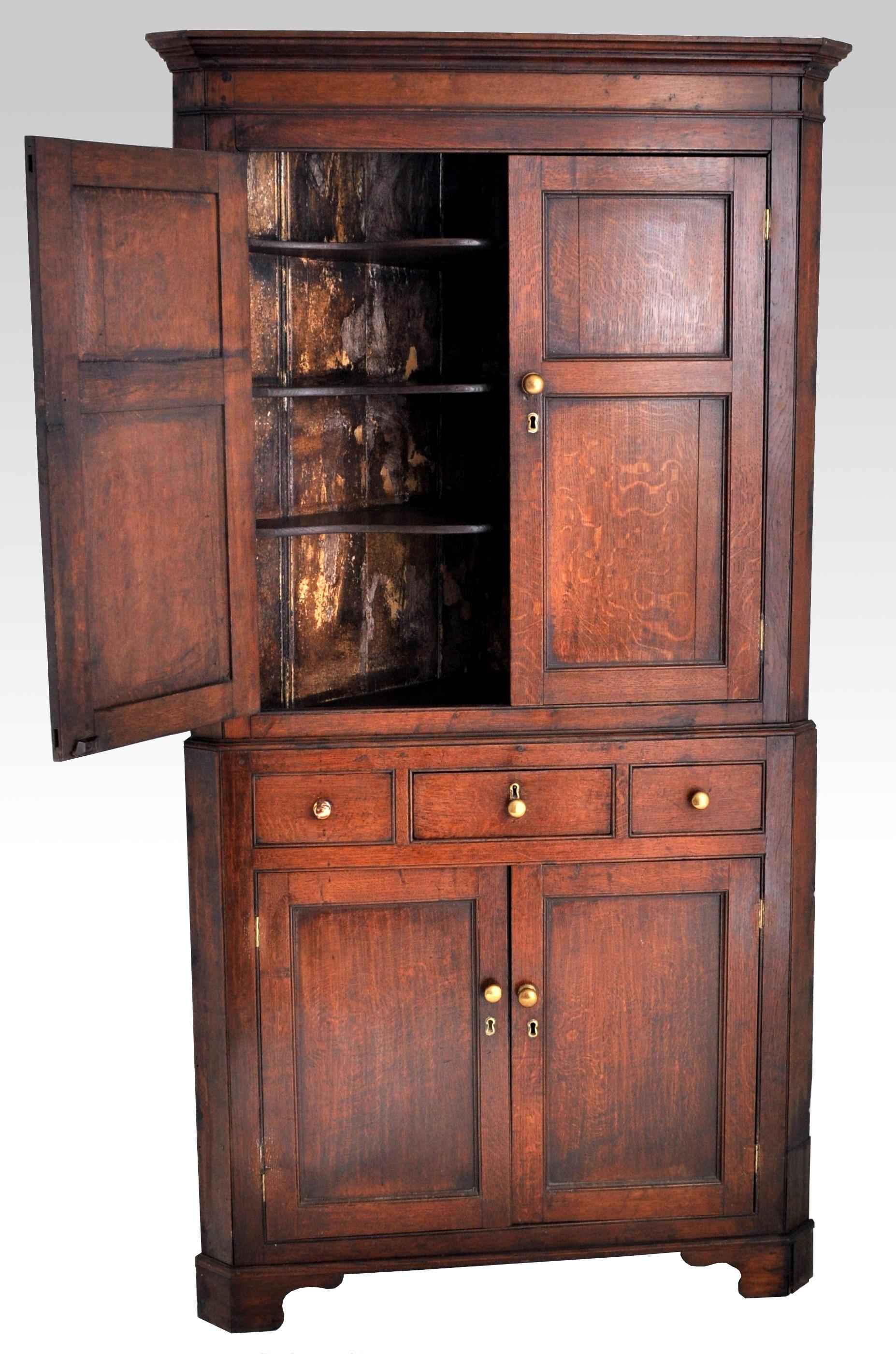 Antique English Georgian George III oak corner cabinet, circa 1780. The cabinet in two sections and having a stepped crown to the top, the top section having twin fielded paneled doors and enclosing three shaped shelves. The base having a central