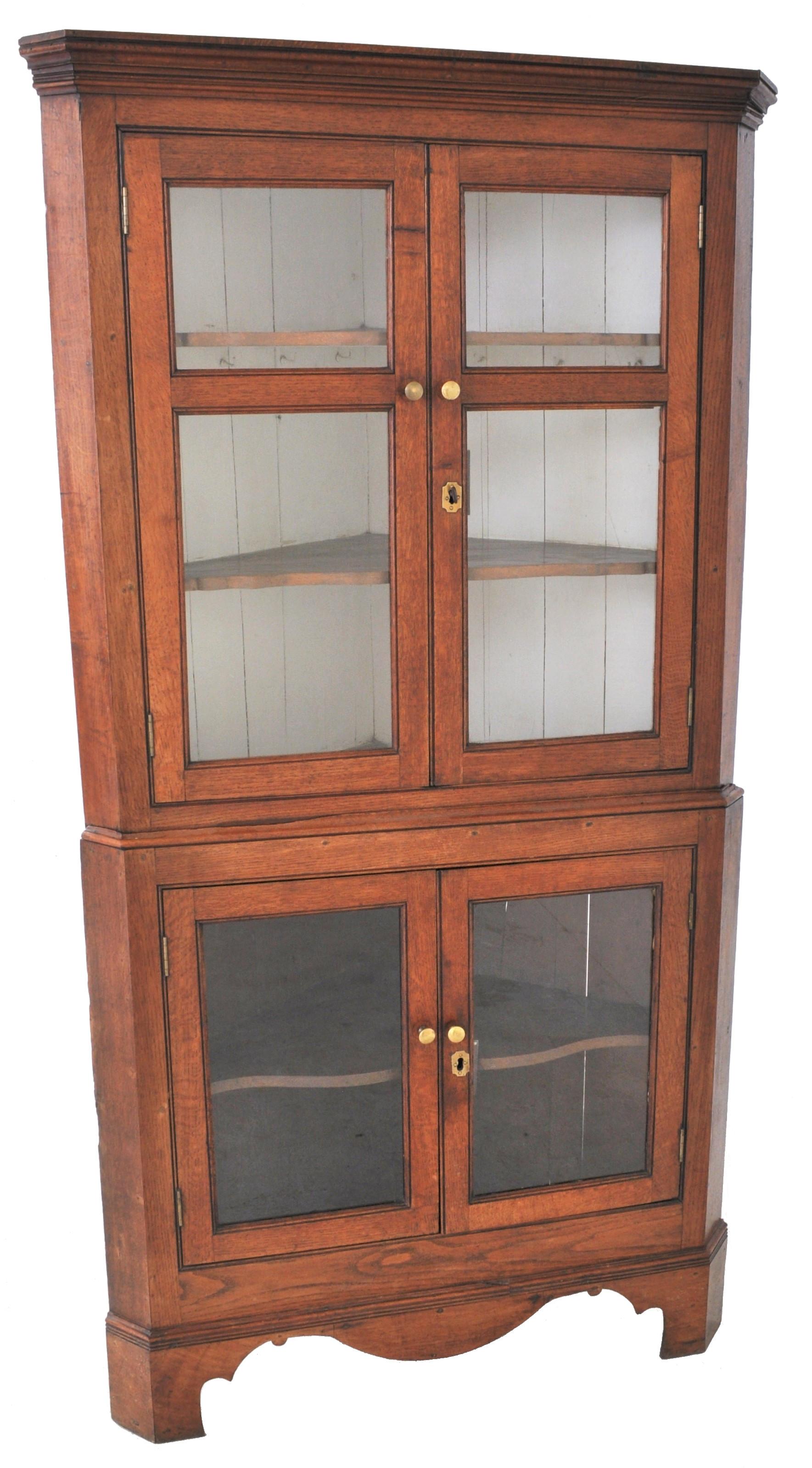 Antique English Georgian George III oak corner cabinet, circa 1800. The two-sectioned cabinet having a stepped cornice to the top with twin doors below enclosing two shaped shelves. The base also having twin doors and enclosing a single shelf, the