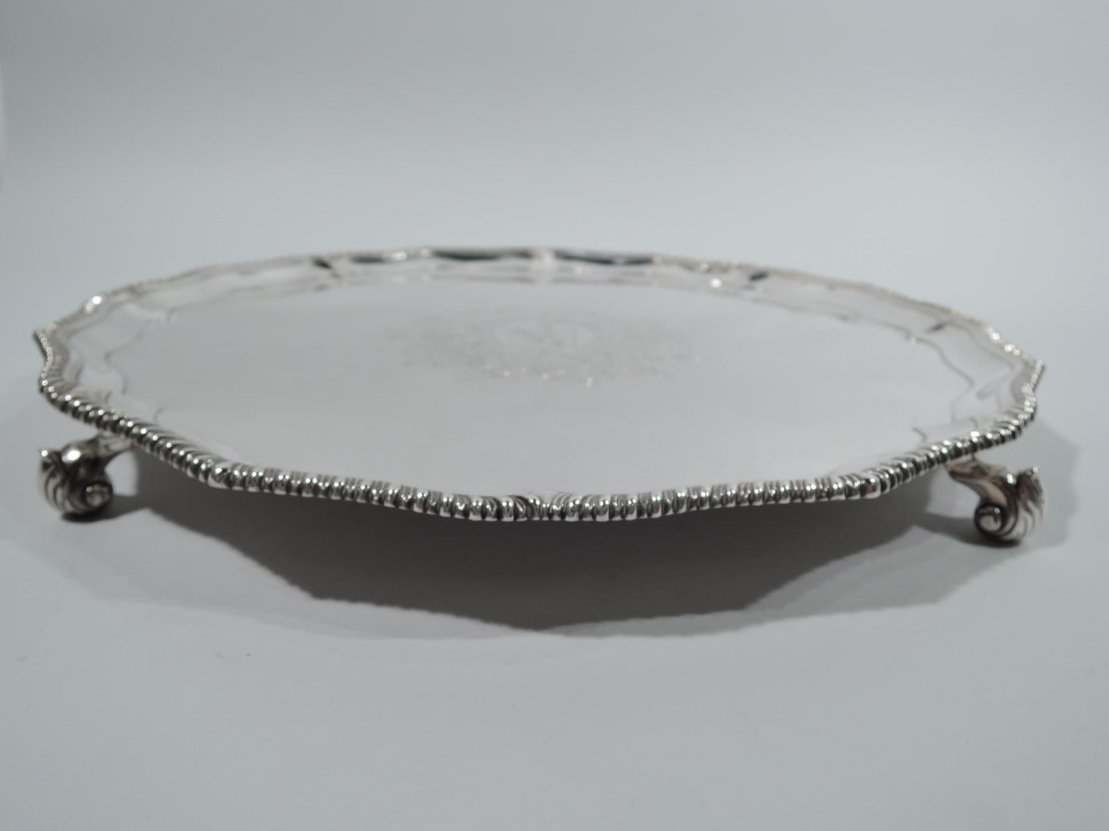 George III sterling silver salver. Made by Robert Rew in London in 1769. Round and ogee well with engraved armorial in floral surround. Sides tapering, and rim scrolled and gadrooned. Four leaf-capped volute scrolls. Stylish midcentury Georgian.