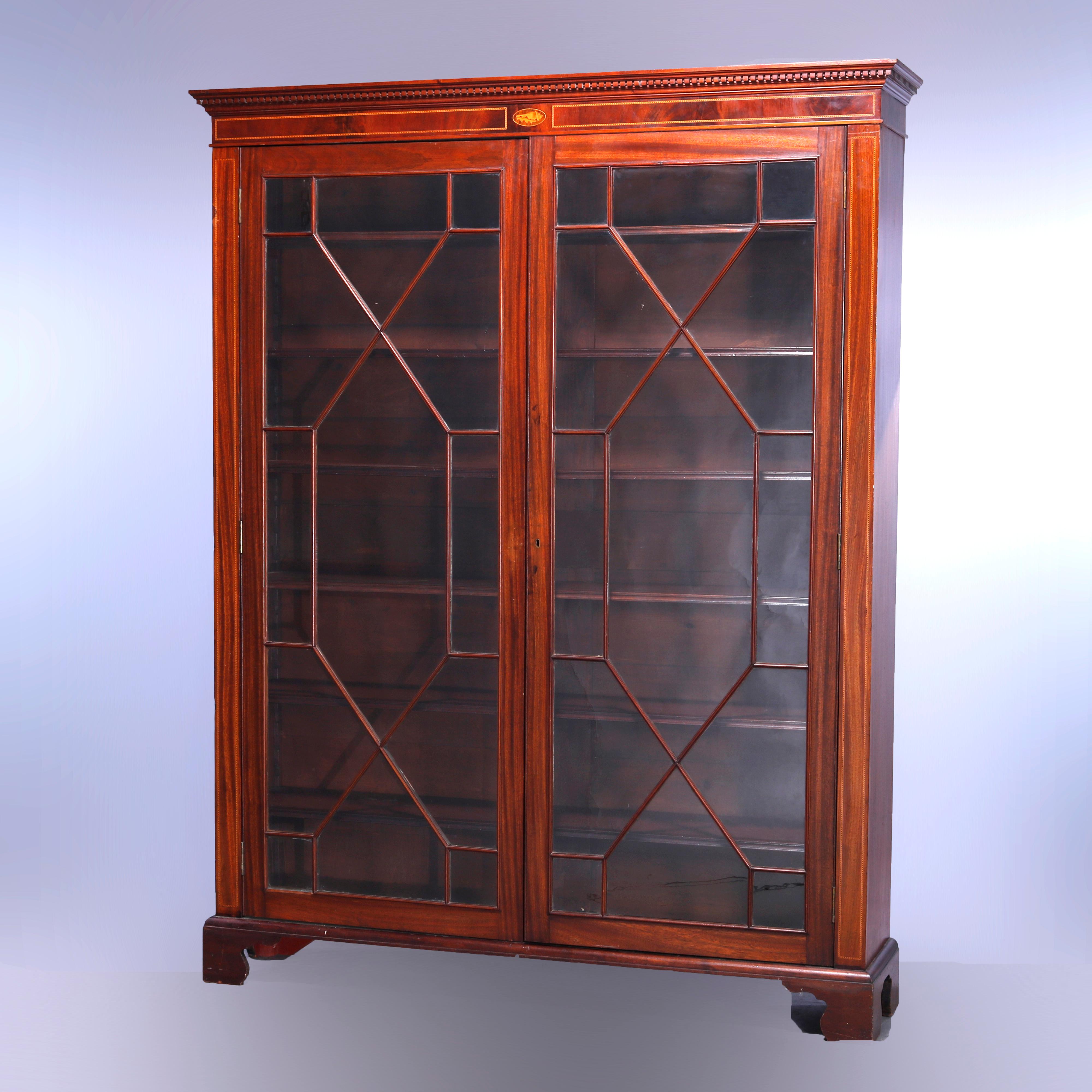 An antique English Georgian enclosed bookcase offers deeply striated mahogany construction with frieze having dental molding over satinwood inlaid central shell with flaking dental banded reserves surmounting case with double mullioned glass doors